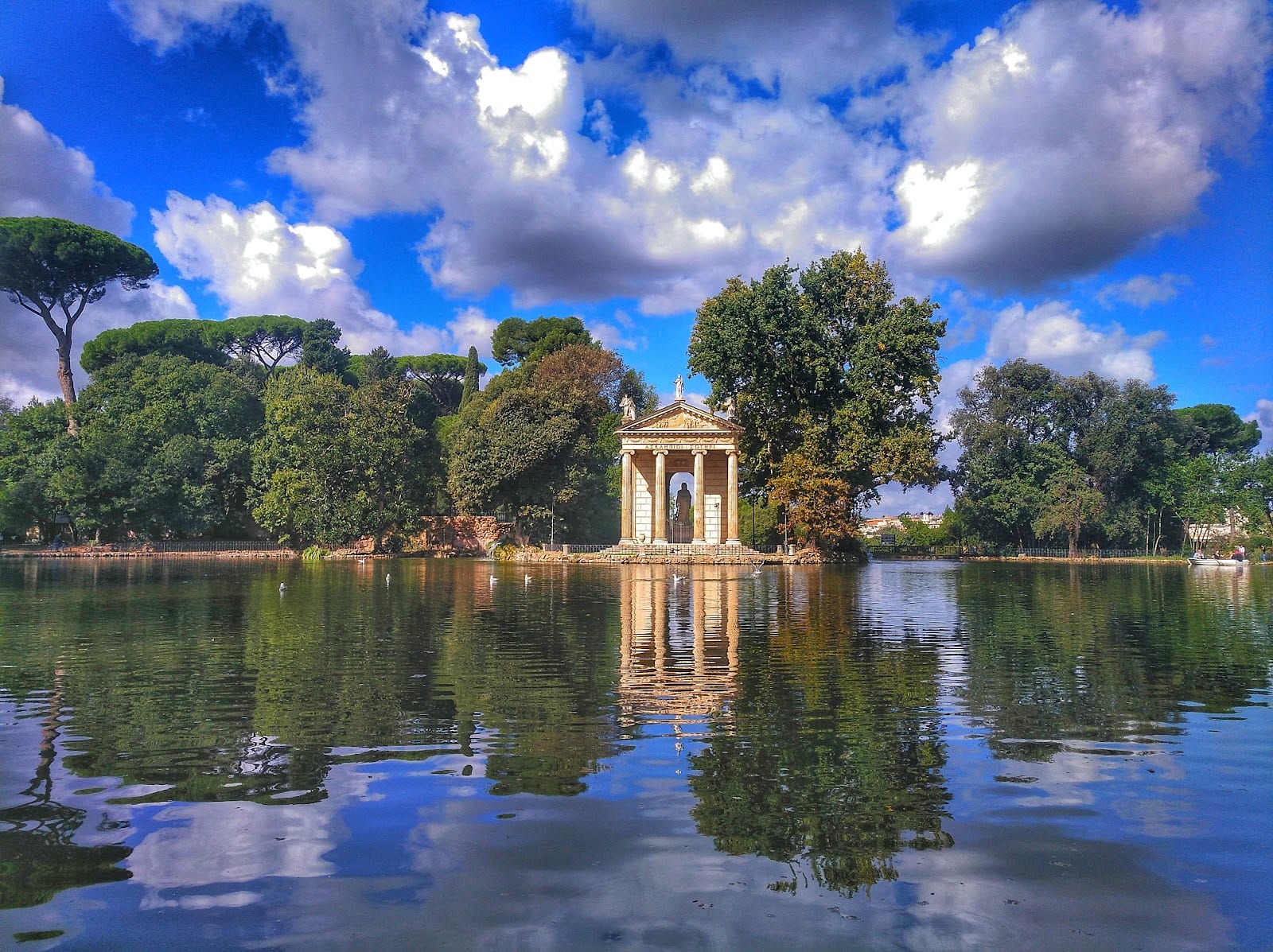 The Temple of Aesculapius reflected in the lake at Villa Borghese, with umbrella pines behind.