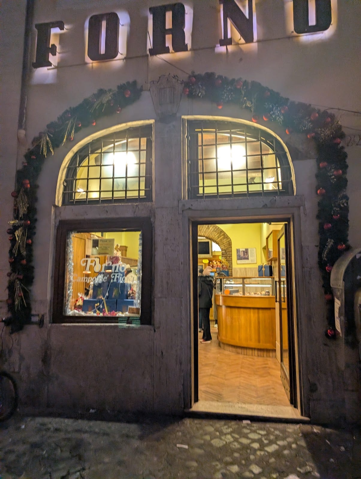 The lit storefront of Forno Campo de' Fiori on the market square.