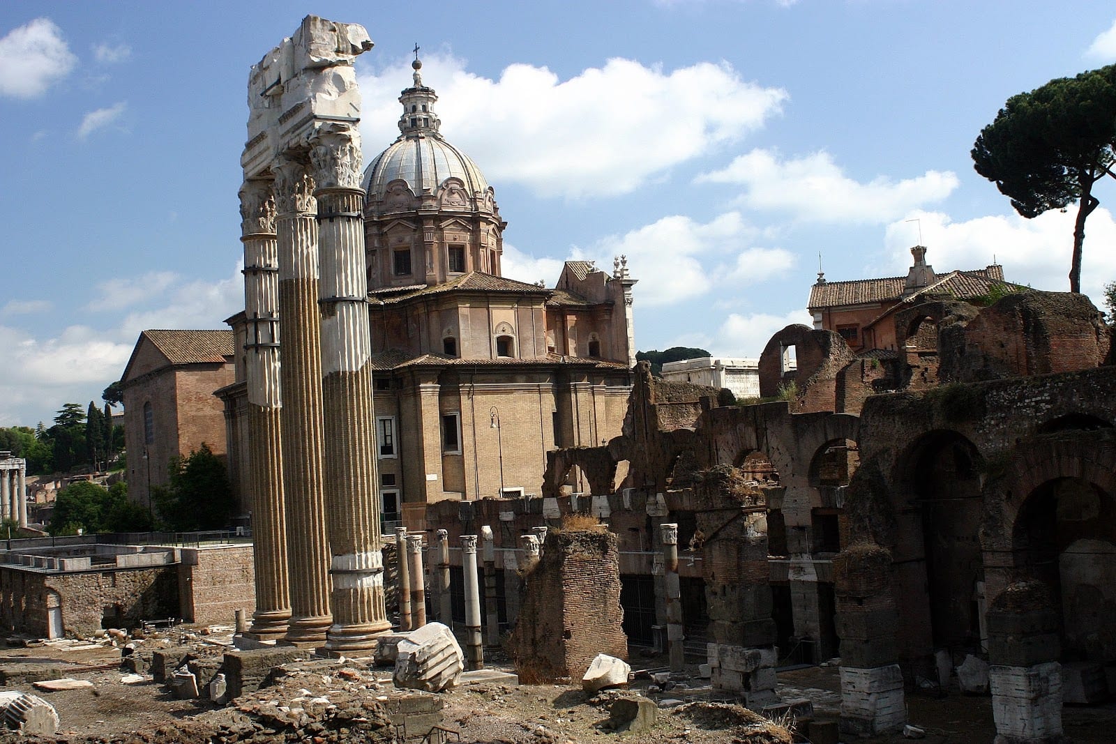 The temple ruins of Largo di Torre Argentina with a church dome behind.