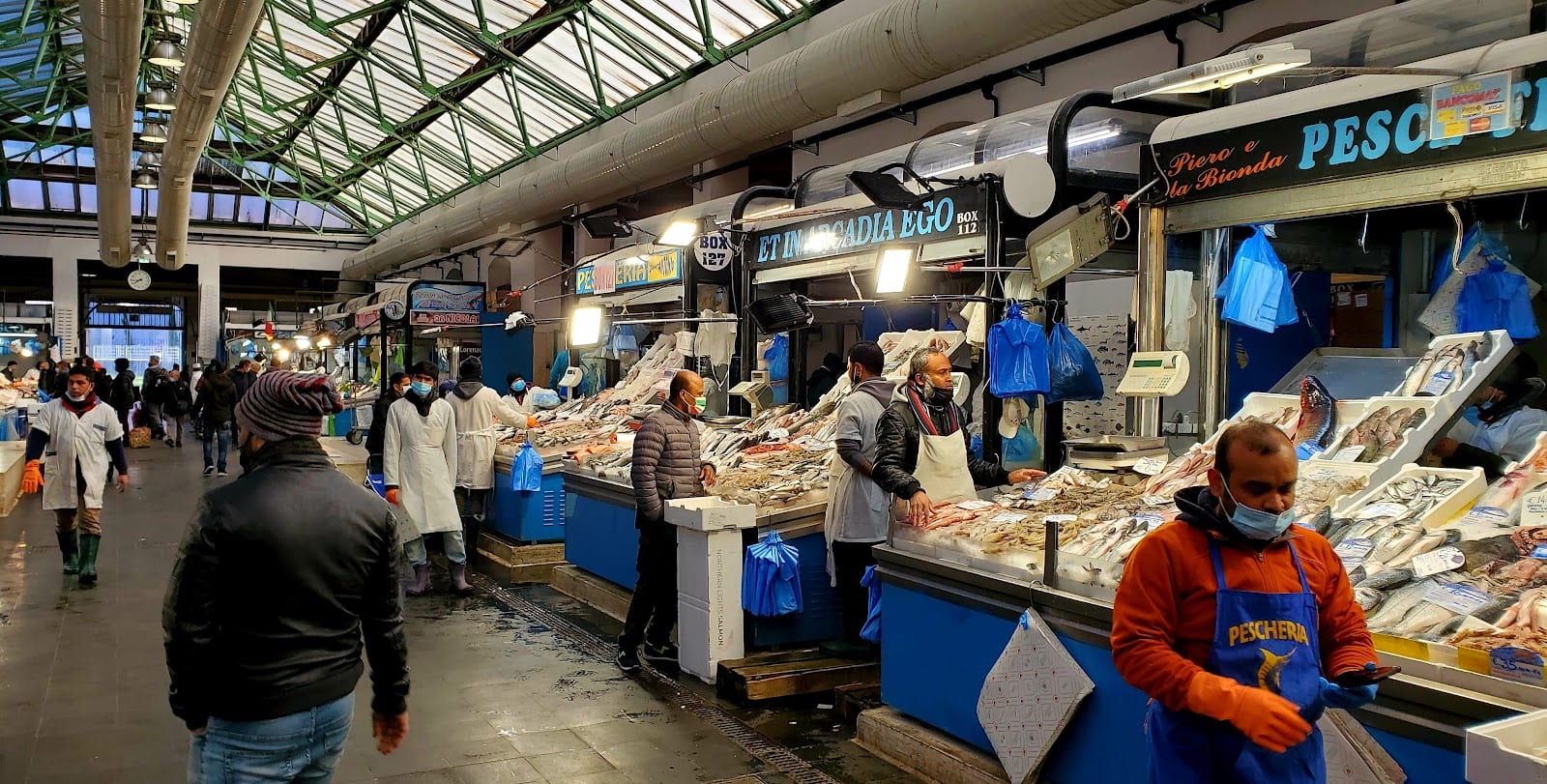 Deli and fish counters with shoppers in the covered Nuovo Mercato Esquilino.