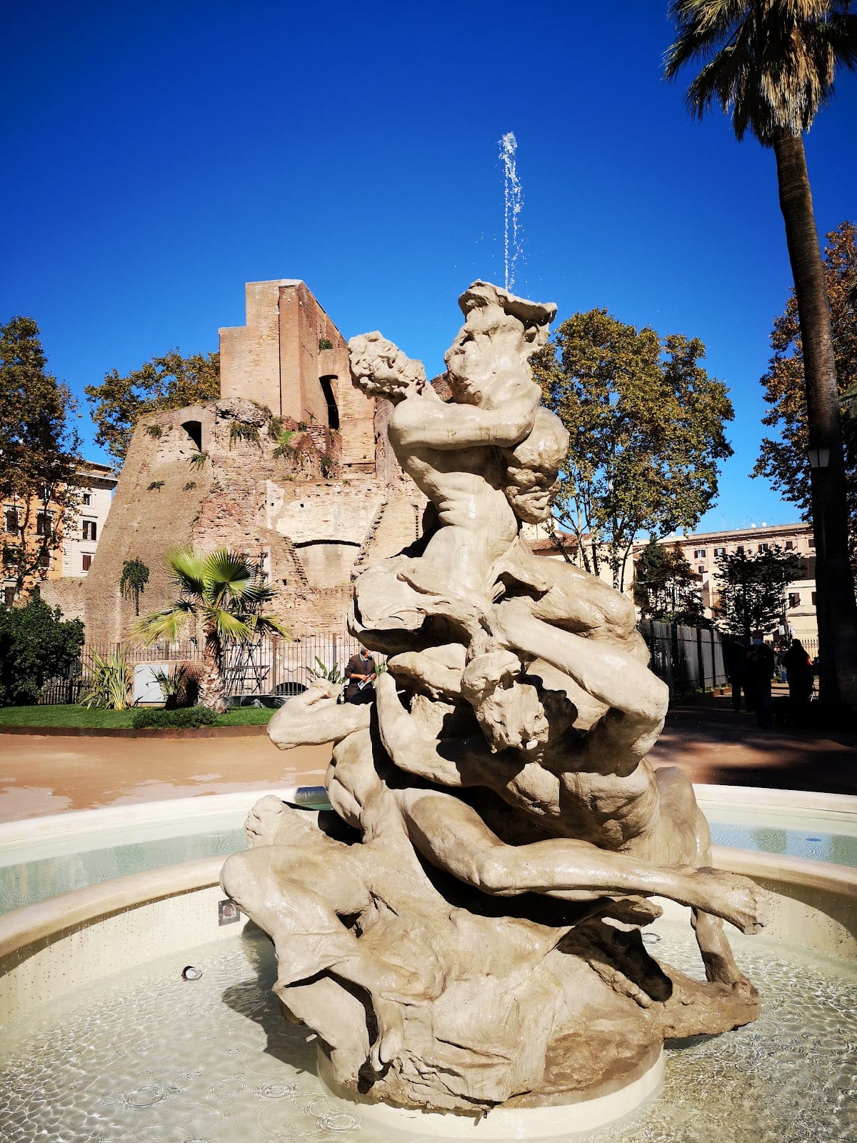 The brick ruin of the Trofei di Mario fountain and a sculpture in the garden of Piazza Vittorio.