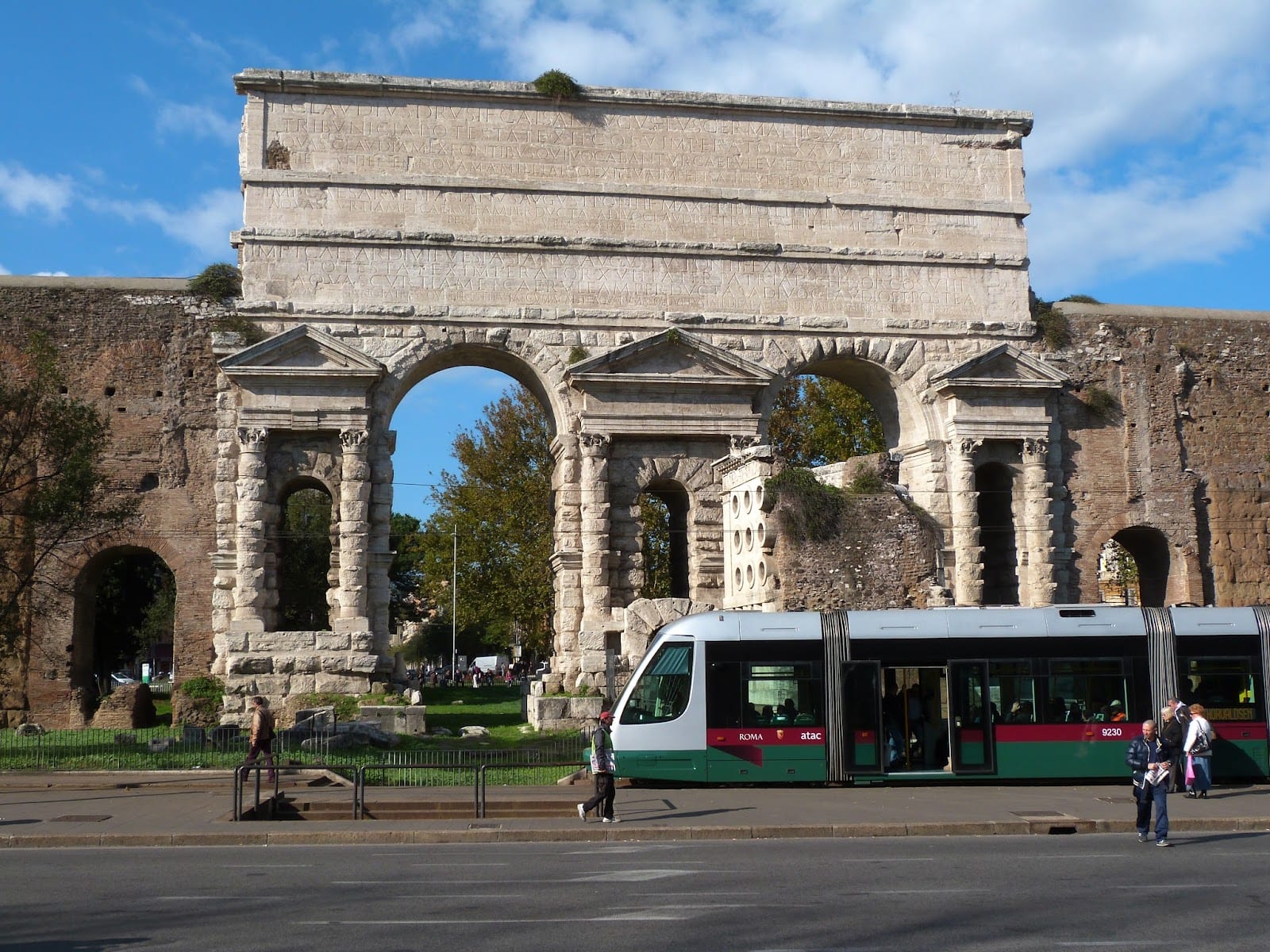 The monumental double travertine arch of Porta Maggiore in Rome with a tram passing.