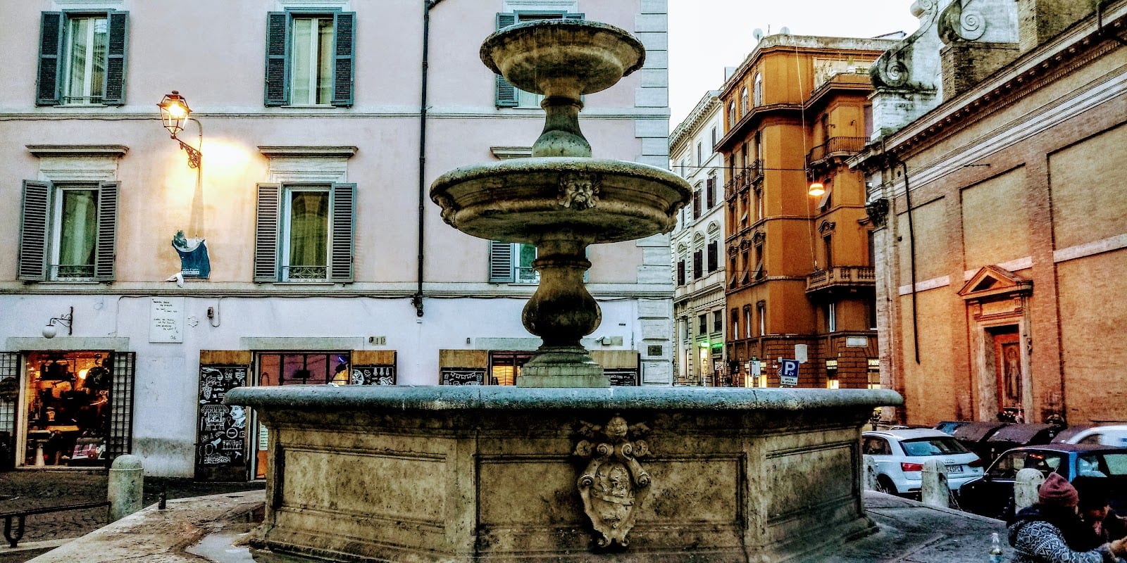 The fountain of Piazza della Madonna dei Monti at dusk, with warm-lit buildings.