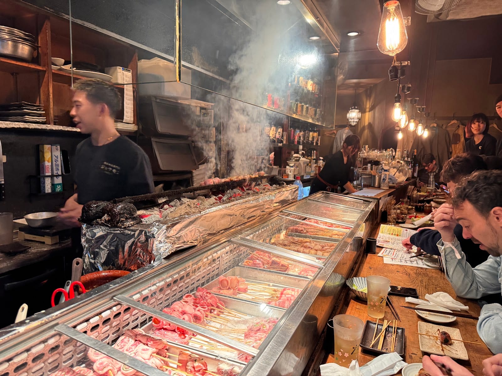 A chef grilling skewers along the counter at Jomon Roppongi.