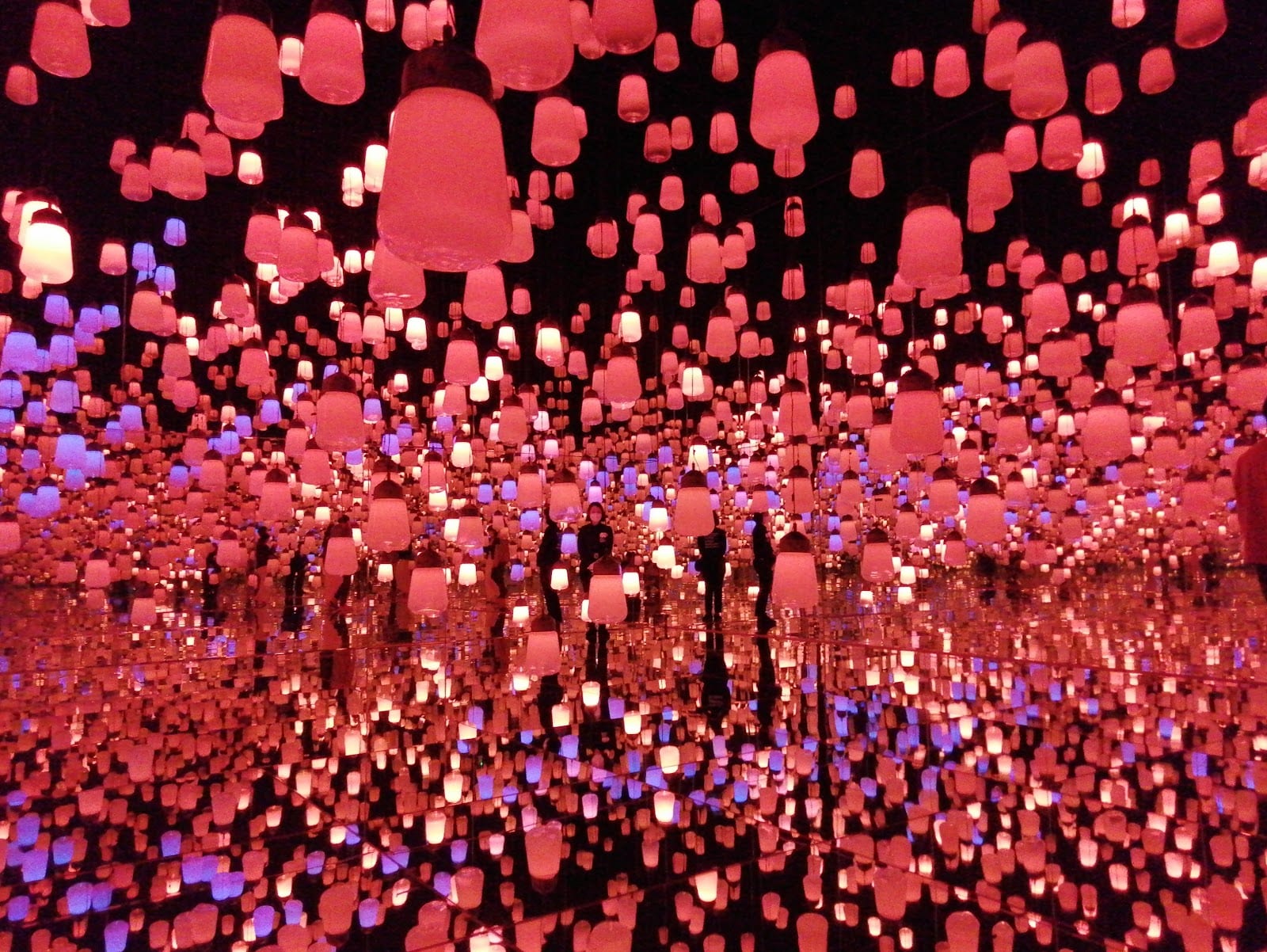 Visitors silhouetted in a room of red hanging lights at teamLab Borderless.
