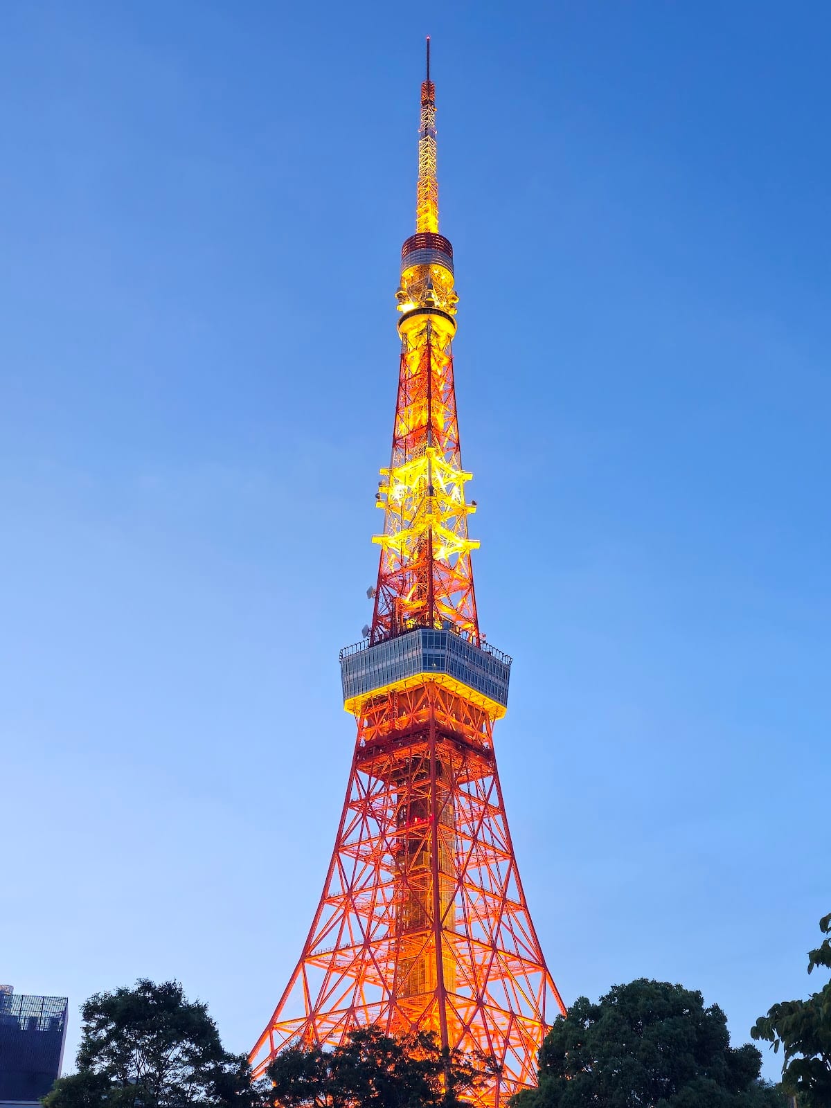 The top of Tokyo Tower lit gold against a blue dusk sky.