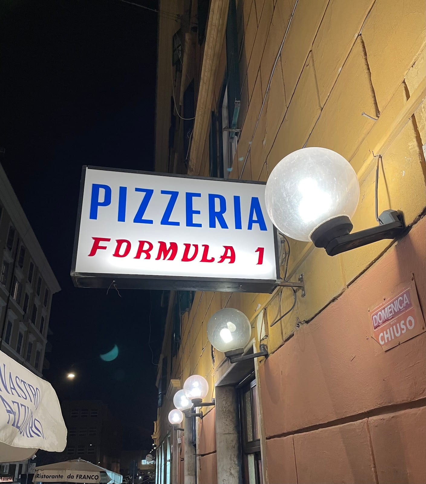The lit Pizzeria Formula 1 sign at night in San Lorenzo.
