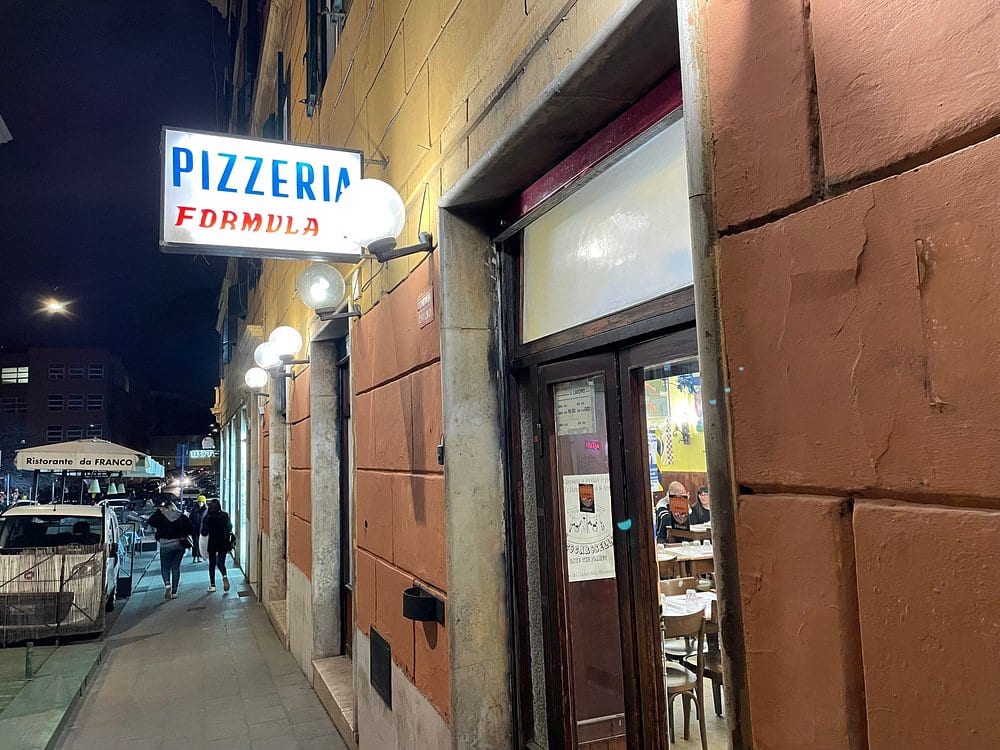 The Pizzeria Formula 1 storefront on Via degli Equi at night.