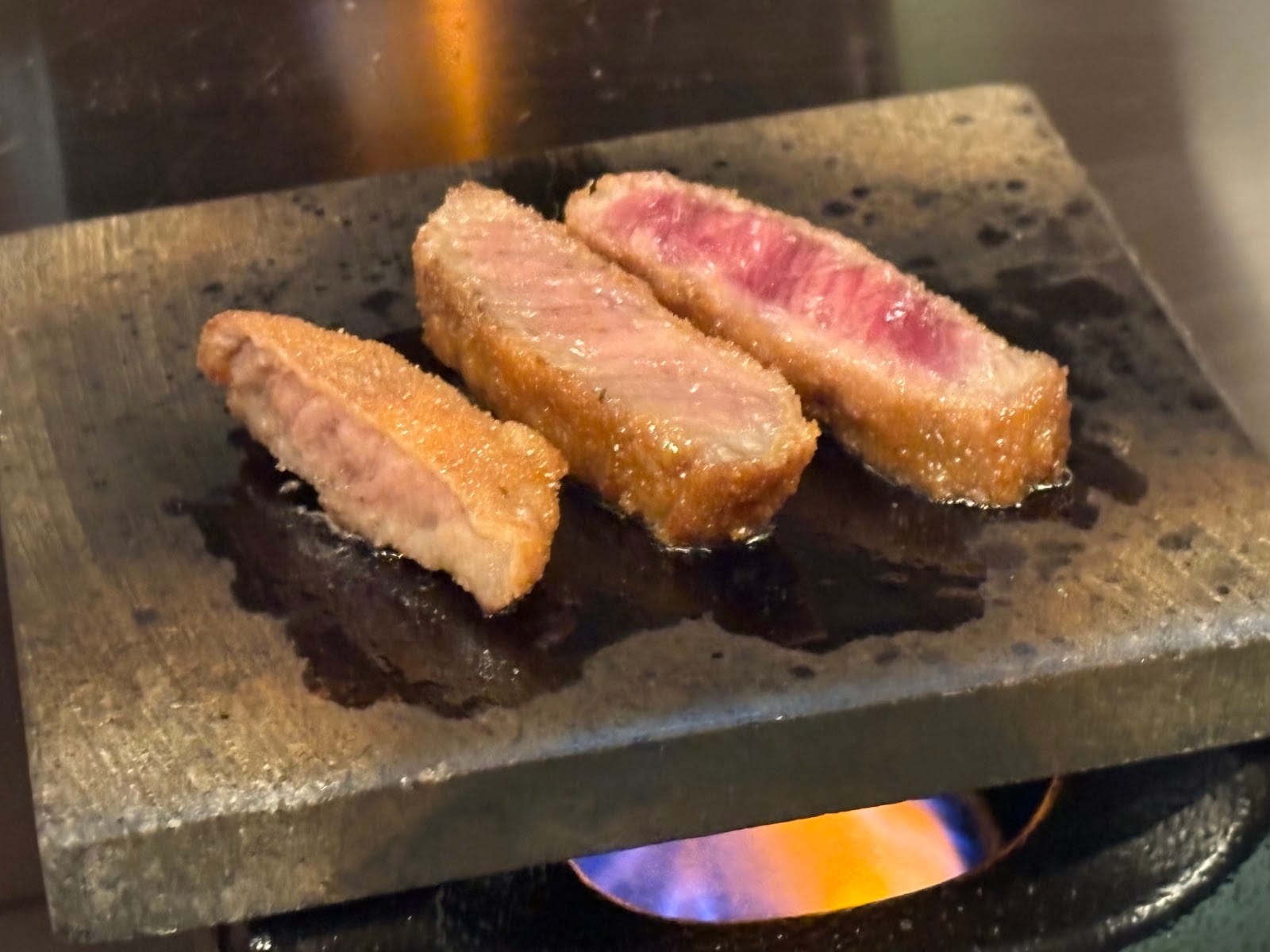 A slice of beef cutlet seared on a hot stone at Gyukatsu Motomura.