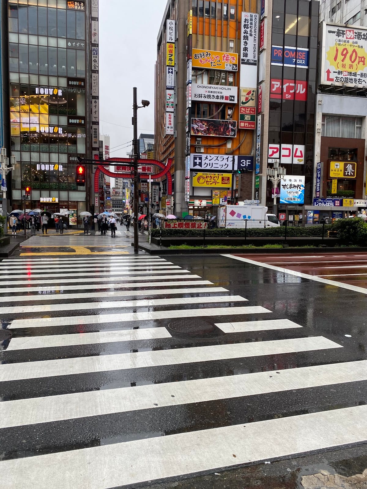 The Kabukicho gate seen across a rain-slicked crossing.