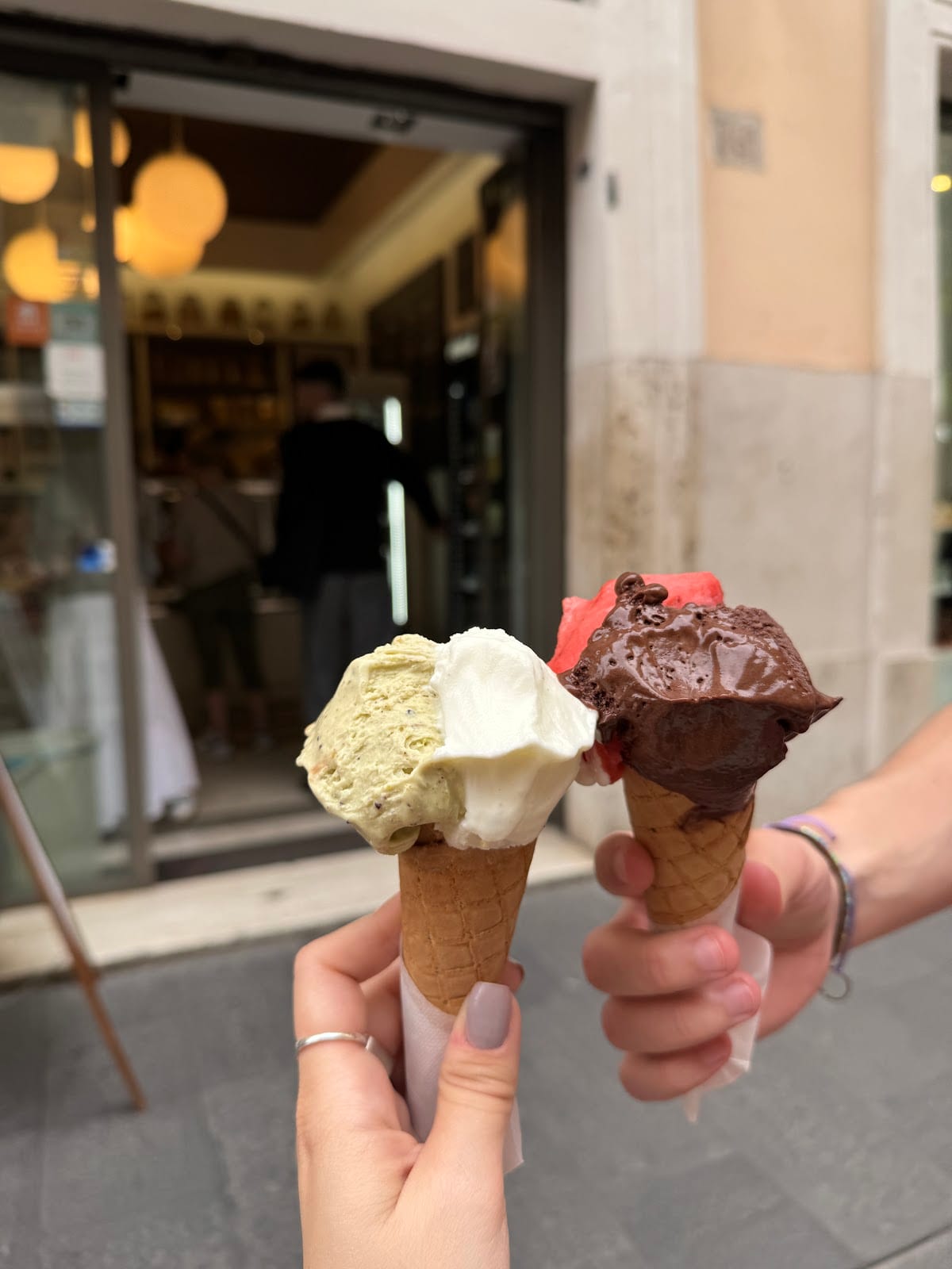 Two cones of gelato held up outside Gelateria dei Gracchi.