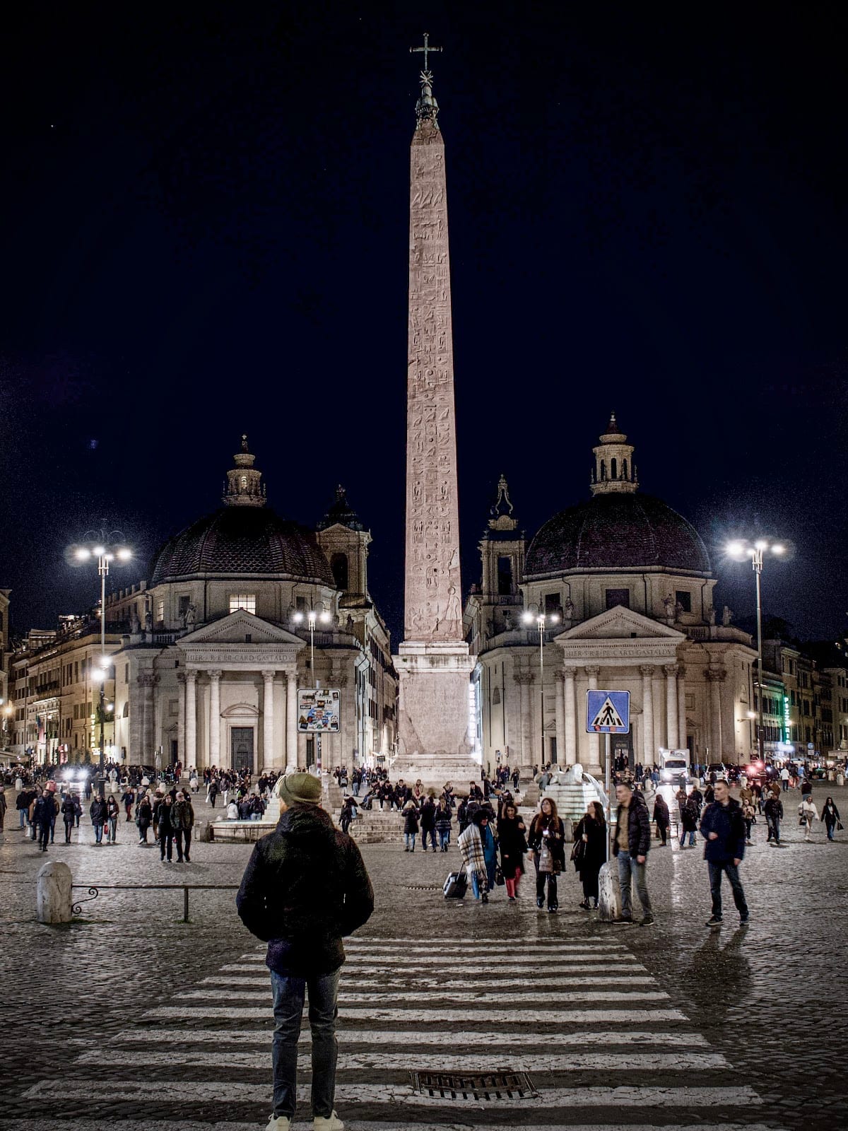 The twin churches and obelisk of Piazza del Popolo lit at night.