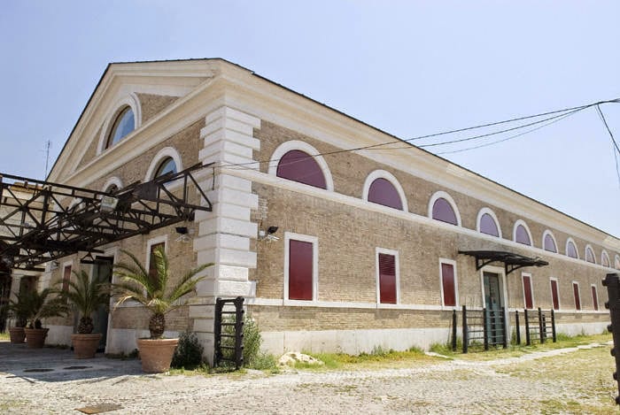 A long brick pavilion with an iron canopy at the Mattatoio arts complex.