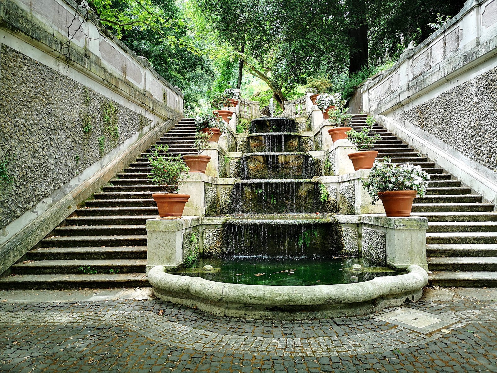 A stepped fountain with potted plants in the Rome Botanical Garden.