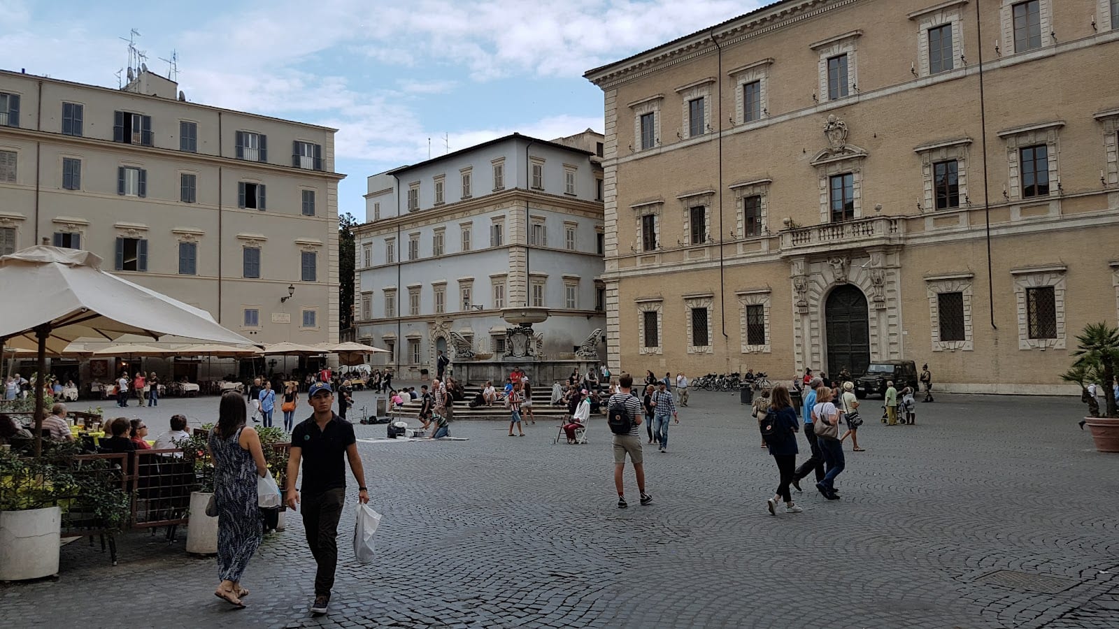 Market stalls and crowds on Piazza di Santa Maria in Trastevere by day.