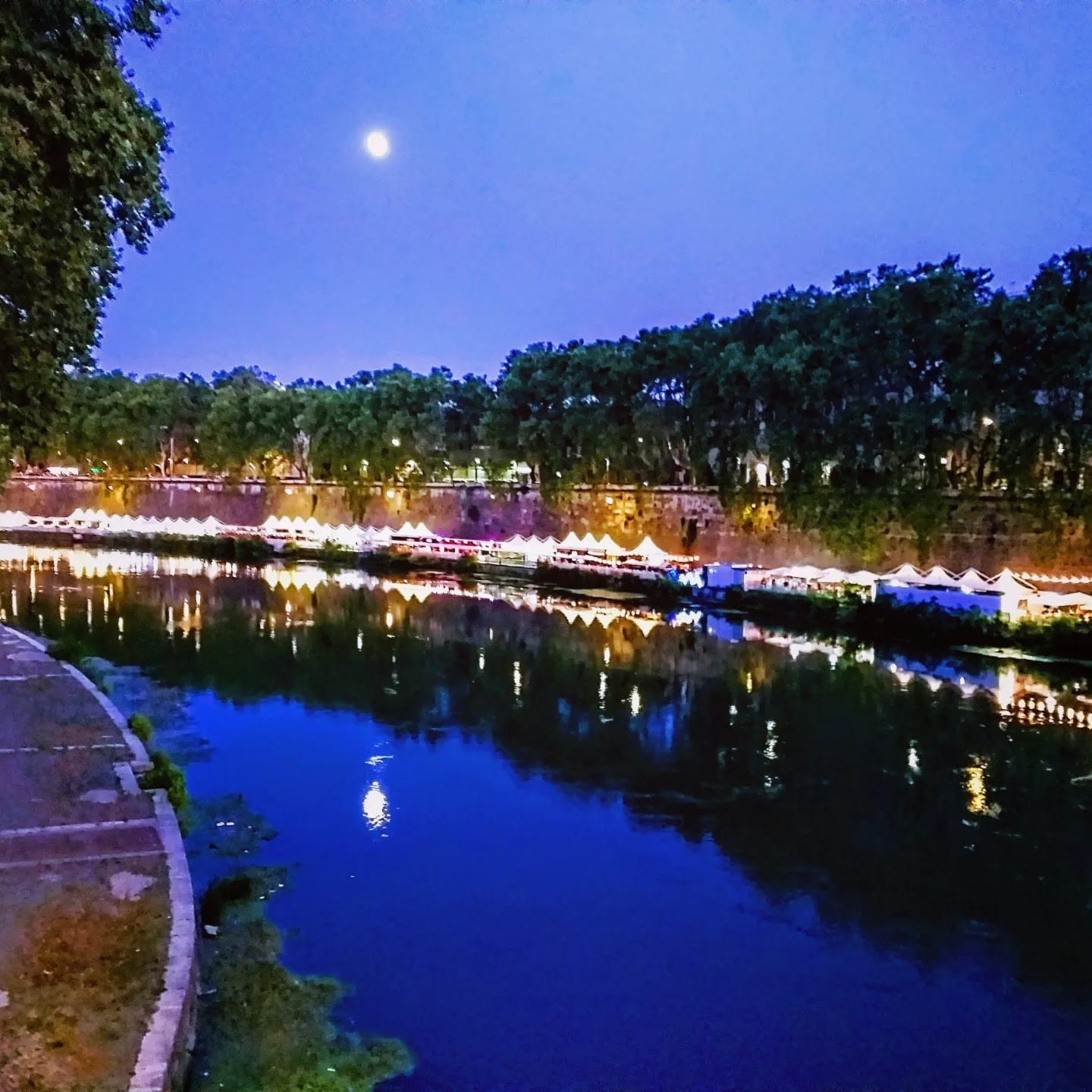 The Tiber riverside near Trastevere lit on a summer evening.