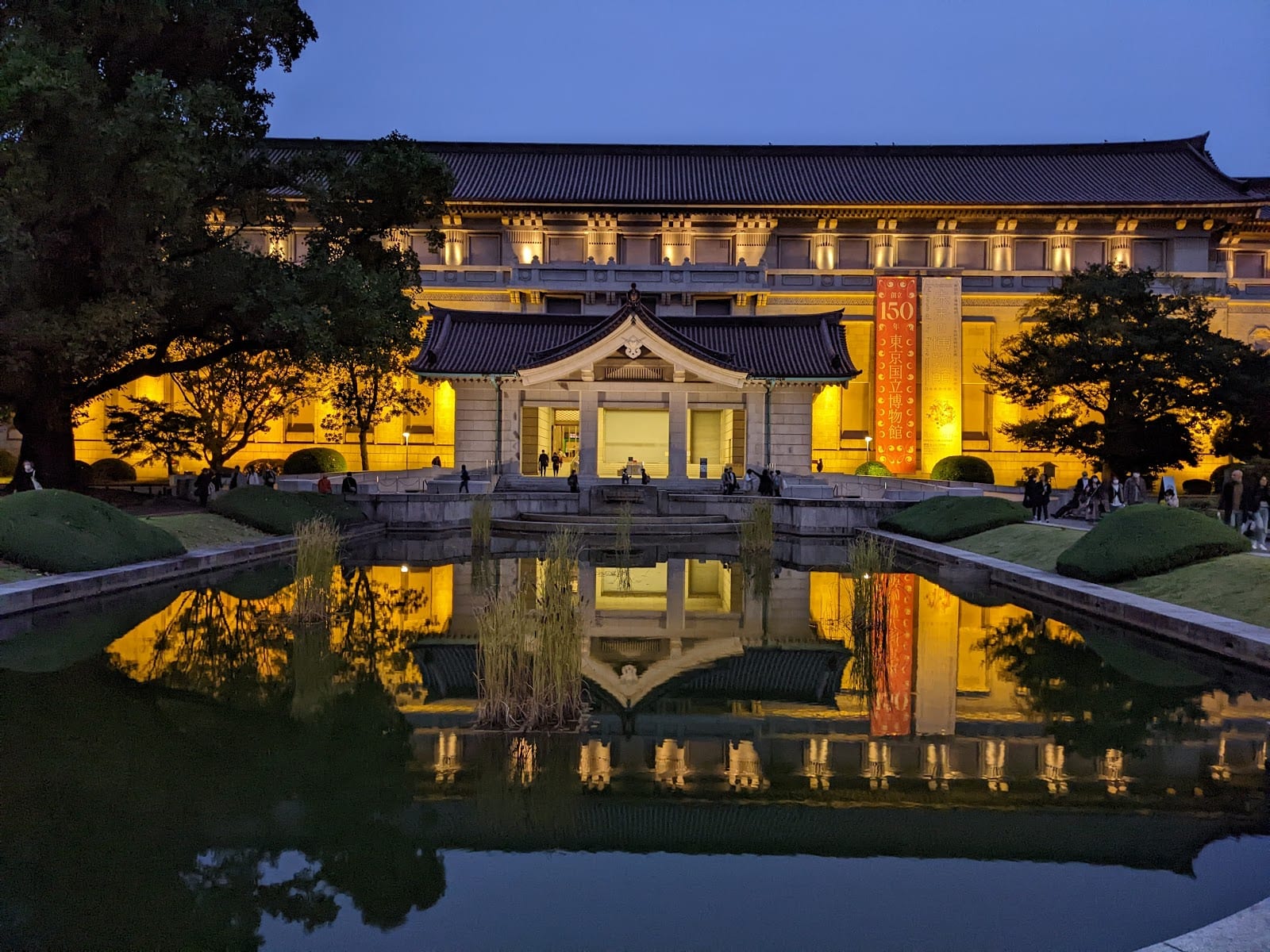 The main Honkan gallery of the Tokyo National Museum lit at dusk, reflected in its pond.