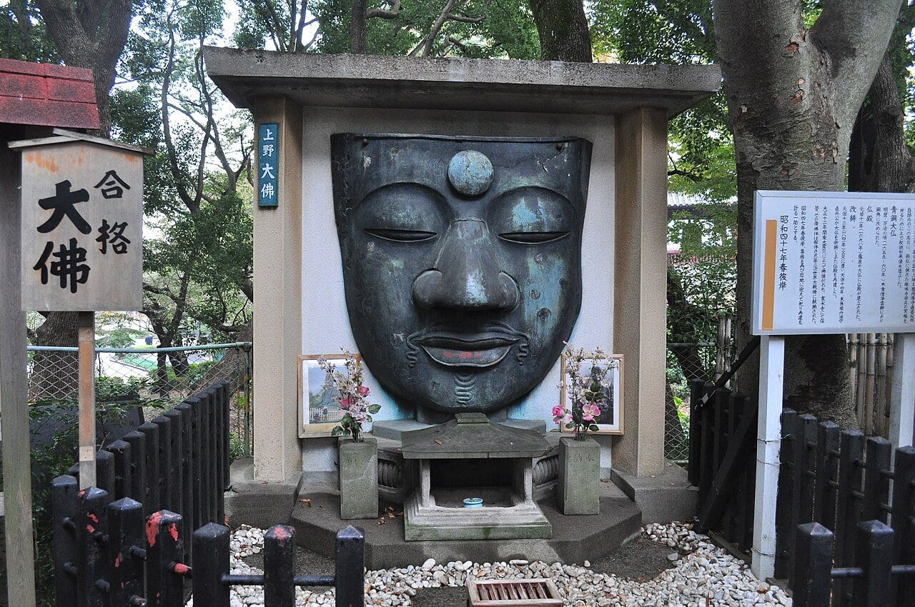 The surviving bronze face of the Ueno Great Buddha, mounted at its original site beside a pass-the-exam sign.