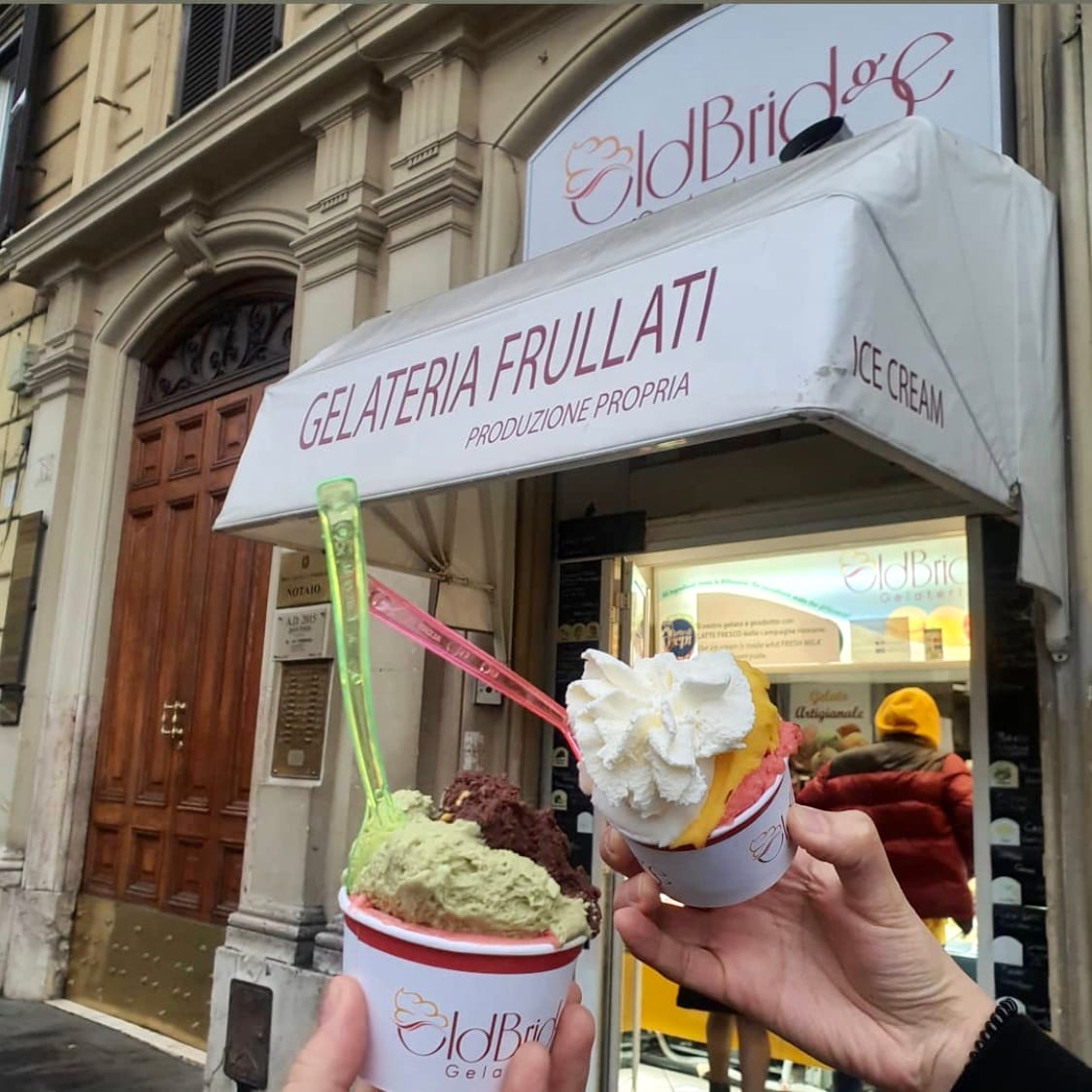 A cup of gelato held in front of the Old Bridge Gelateria storefront.