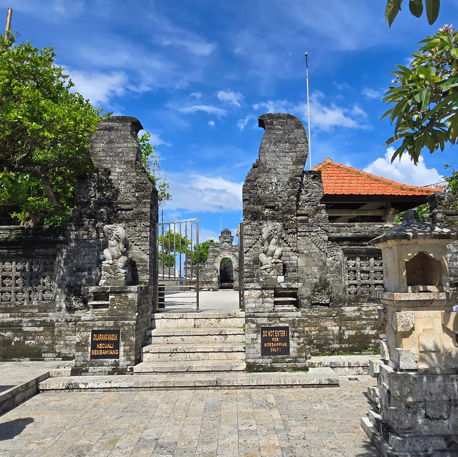 A carved stone gateway and temple buildings at Uluwatu Temple under a blue sky.