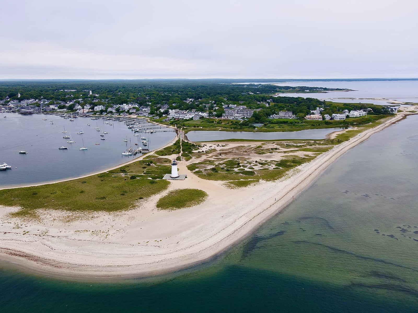 An aerial view of Edgartown Harbor Light on a sandy point beside Edgartown Harbor, with boats and shoreline buildings in the background.