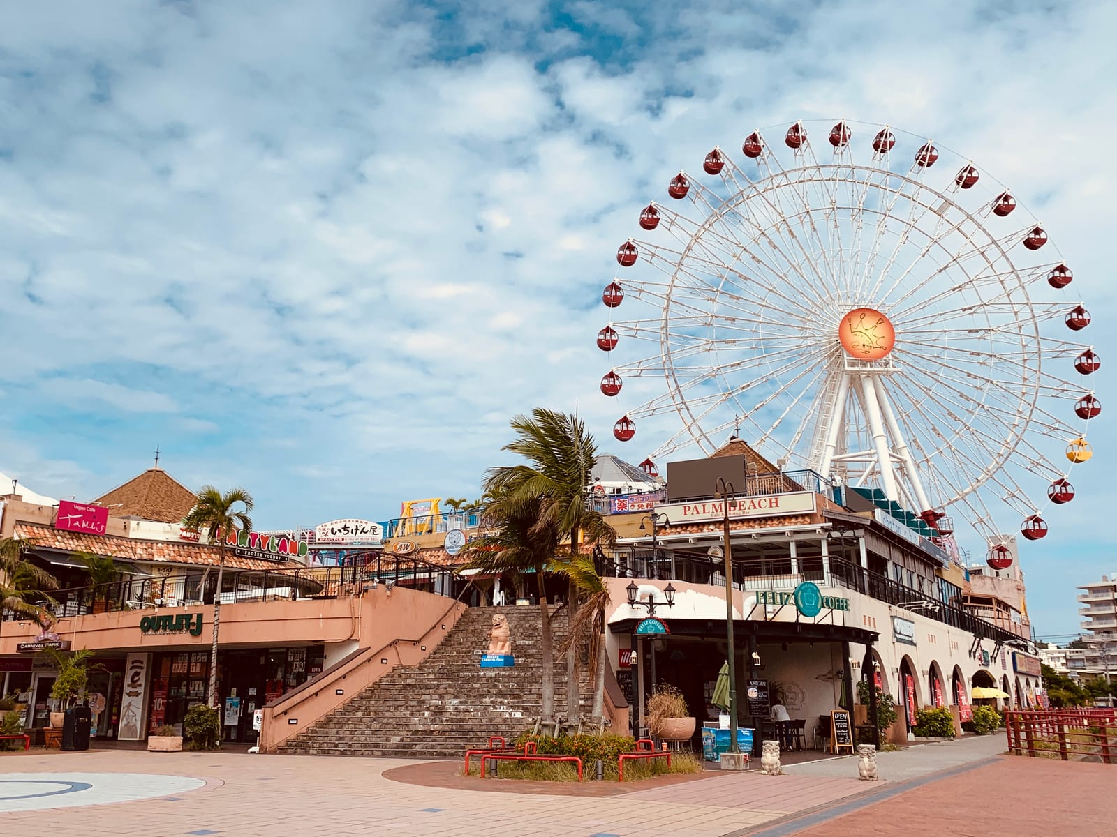 Colorful shops and palm trees fill Mihama American Village beneath a large Ferris wheel in Chatan, Okinawa.