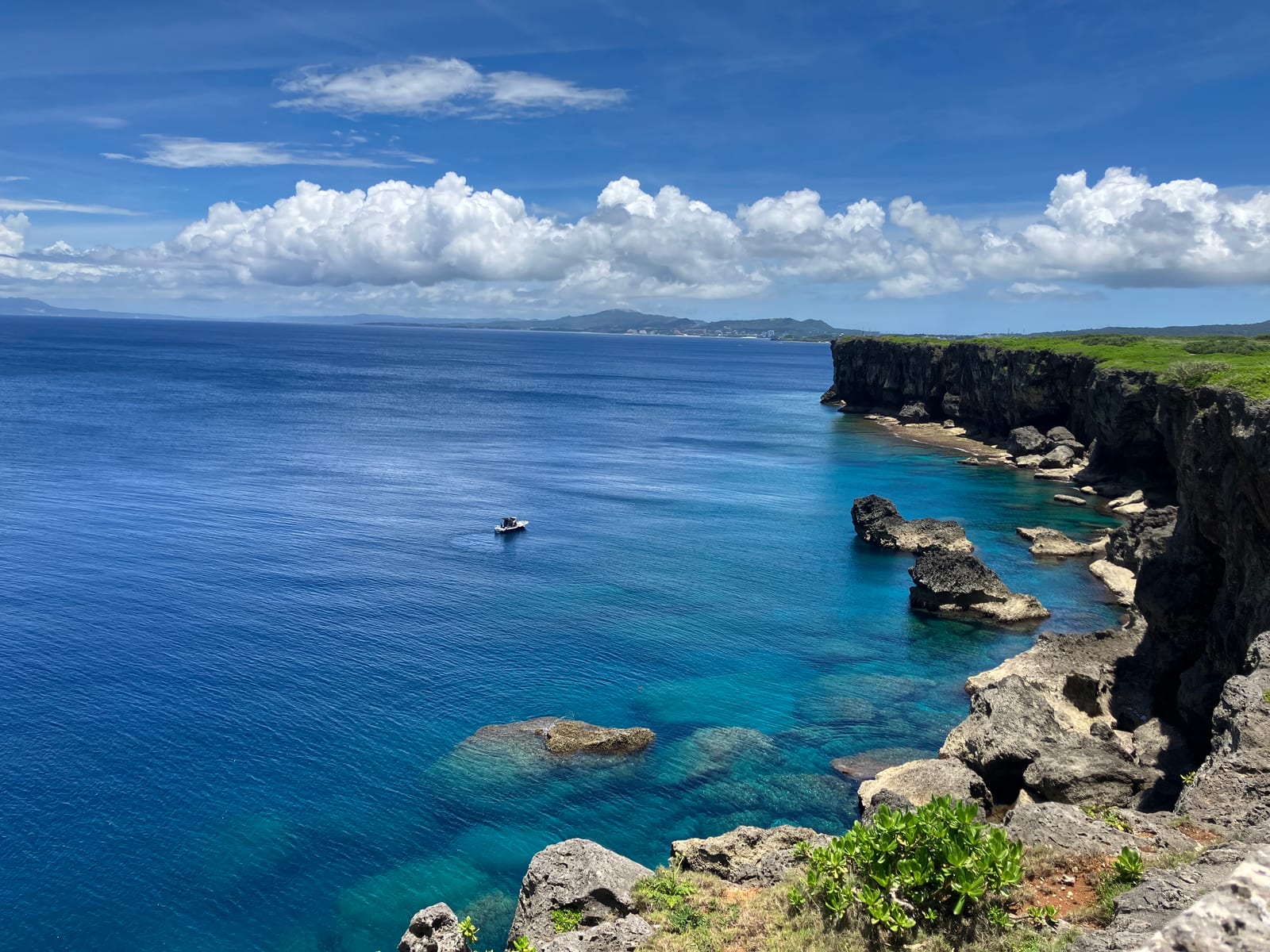 Rocky limestone cliffs at Cape Zanpa above blue ocean, with a small boat offshore.