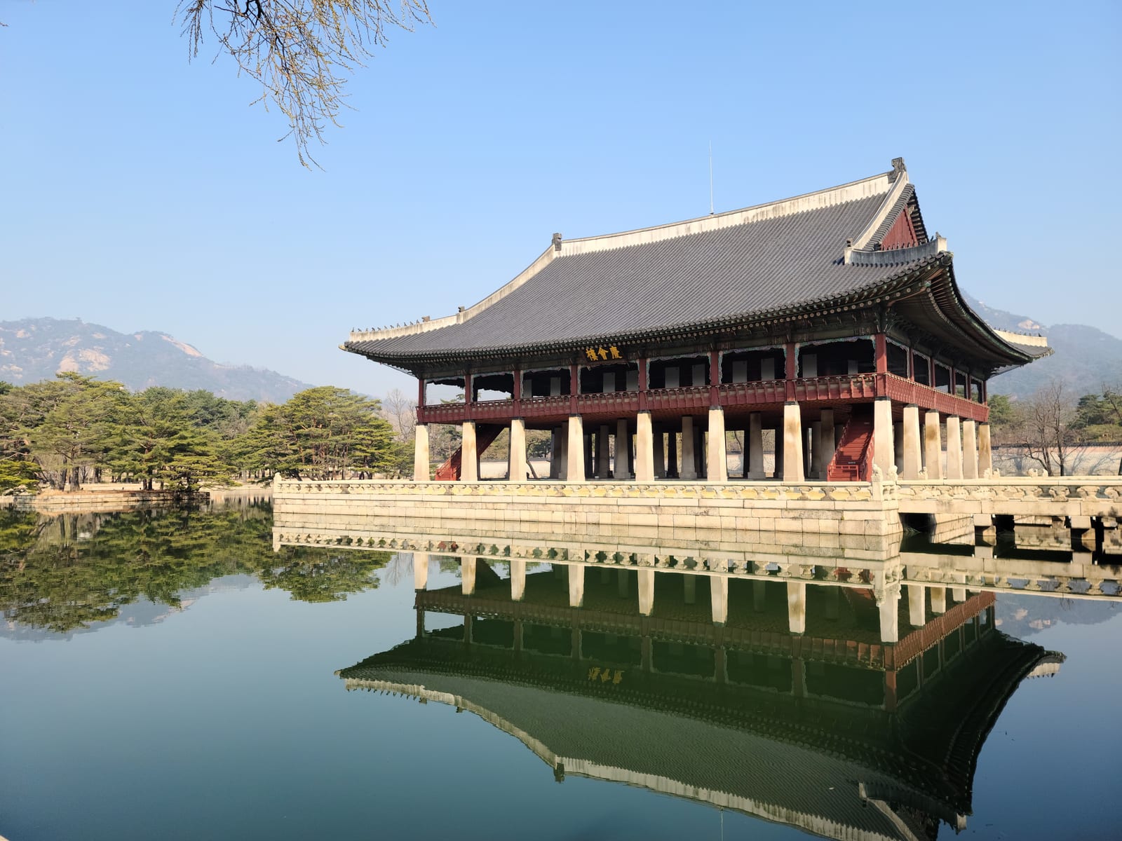 A pavilion at Gyeongbokgung Palace stands beside a pond with mountains behind it and a reflection in the water.