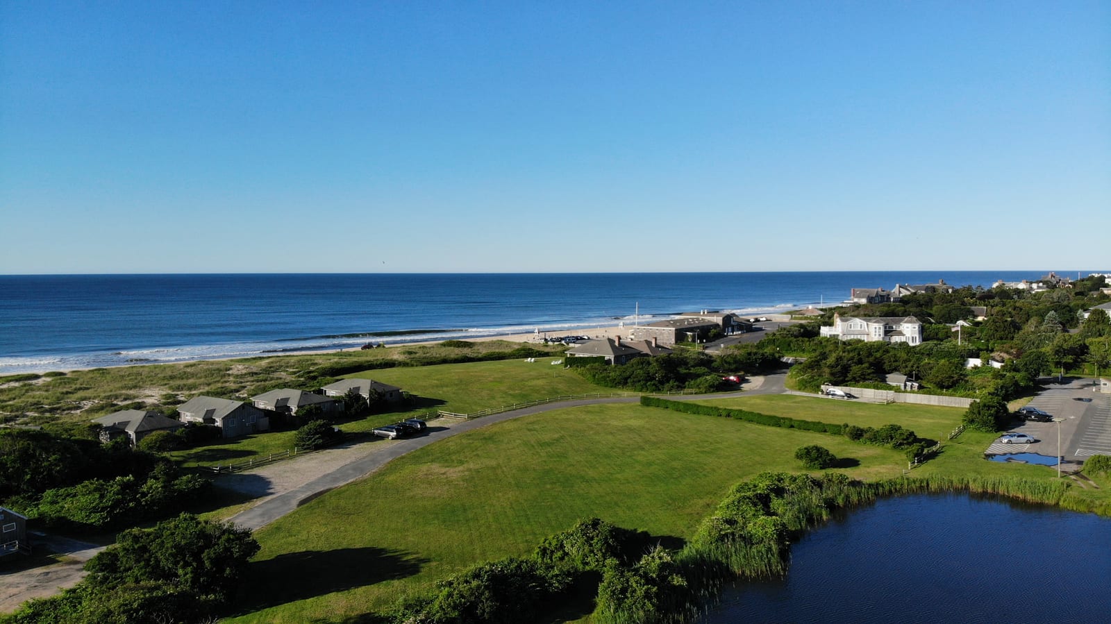 An aerial view of Main Beach East Hampton shows the shoreline, ocean, dunes, nearby homes, and parking area.