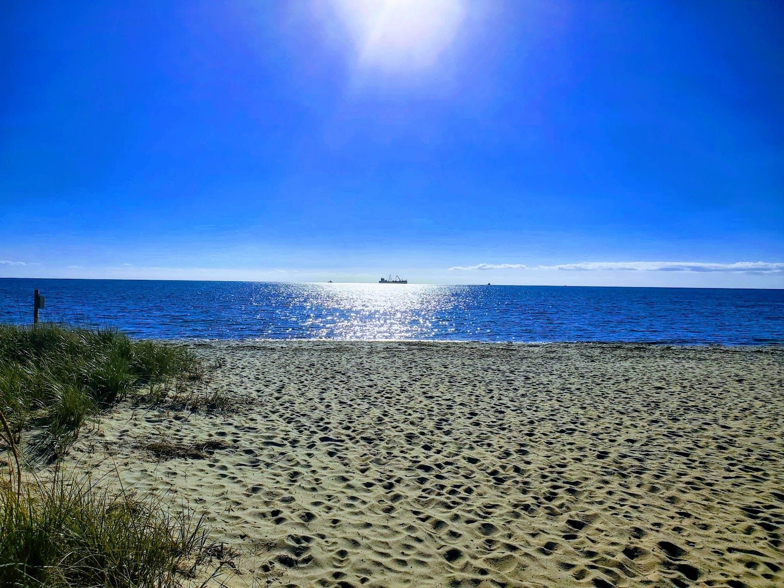 Bright sun over the deep blue Nantucket Sound water and sand at Craigville Beach.