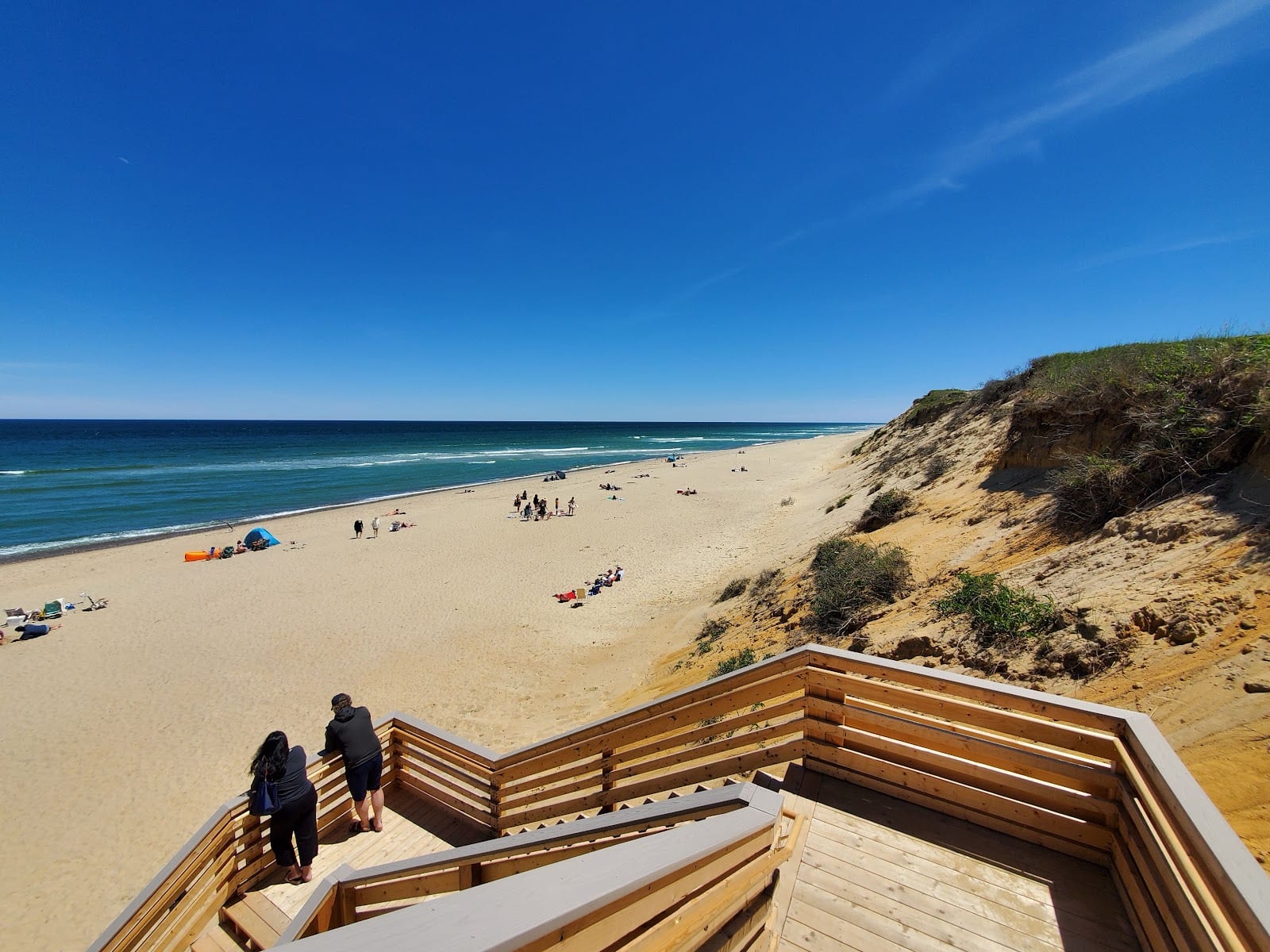 Beachgoers on the sand below the tall sandy bluff and stairs at Marconi Beach.