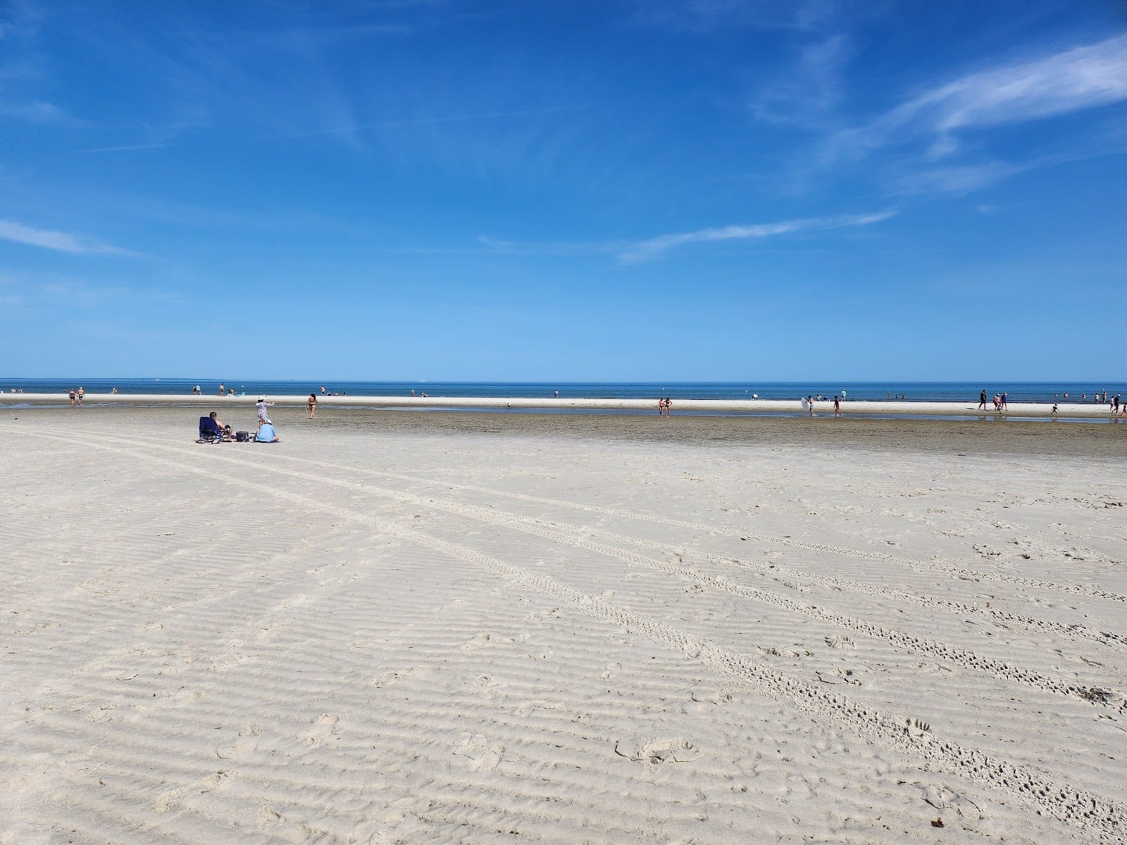 The vast flat sand of Mayflower Beach at low tide under a bright blue sky.