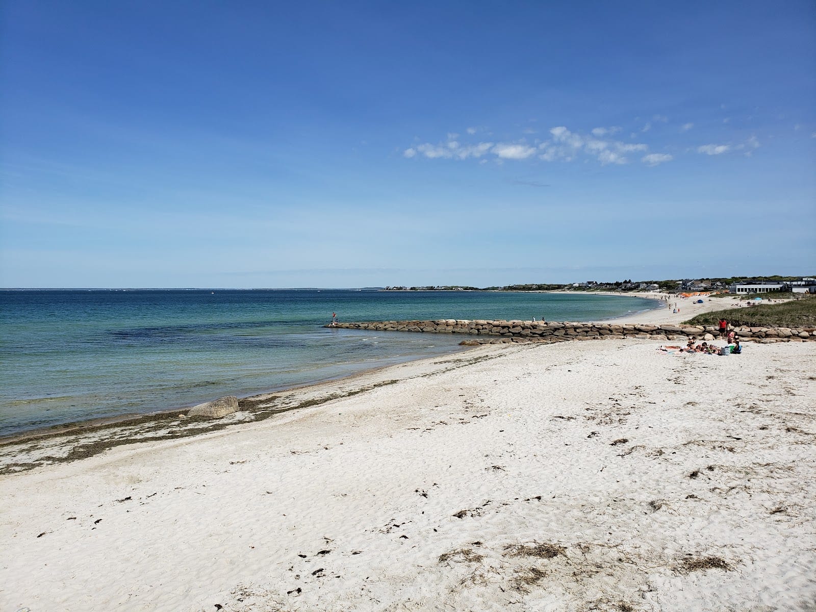Calm shallow water beside a stone groin at Old Silver Beach under a blue sky.