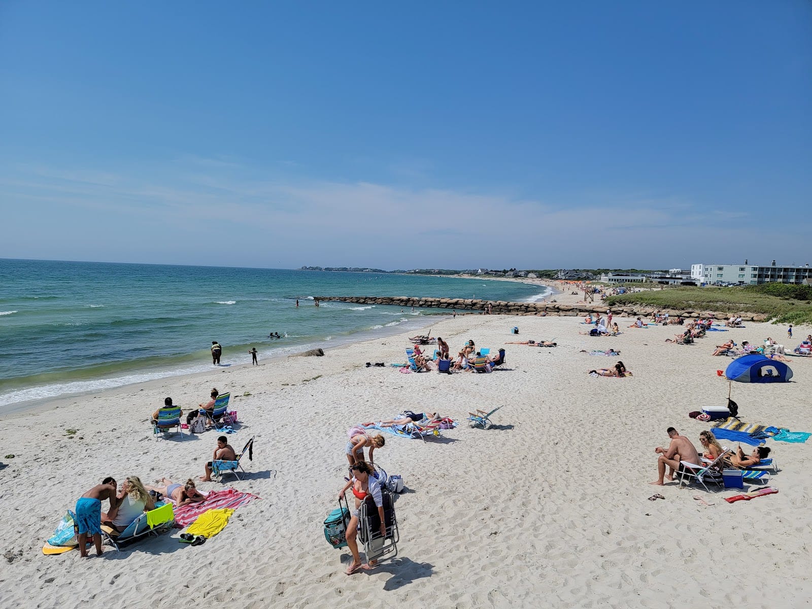 Beachgoers under umbrellas on the sand at Old Silver Beach on a sunny day.