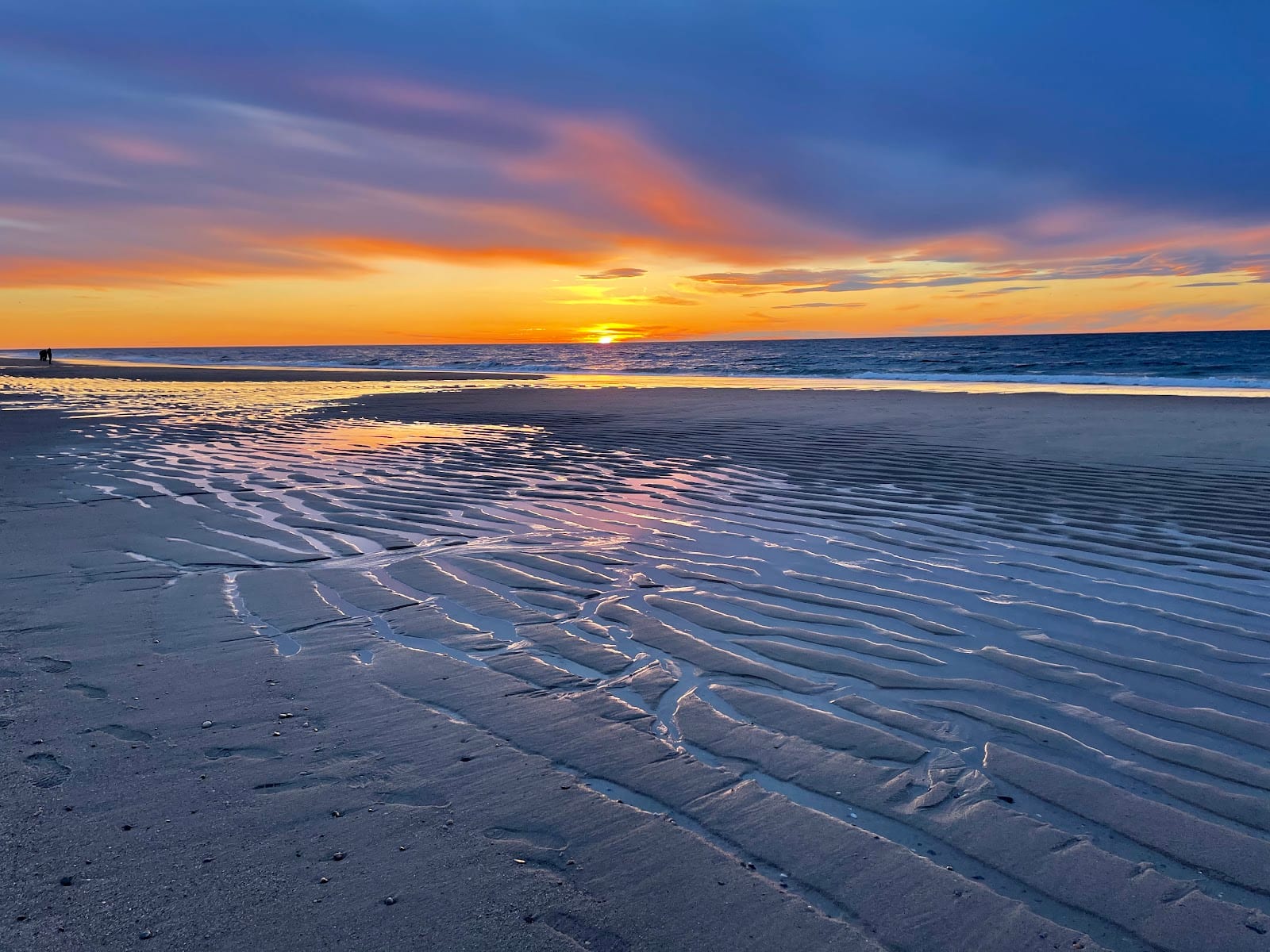 The sun setting over the ocean with rippled wet sand in the foreground at Race Point.