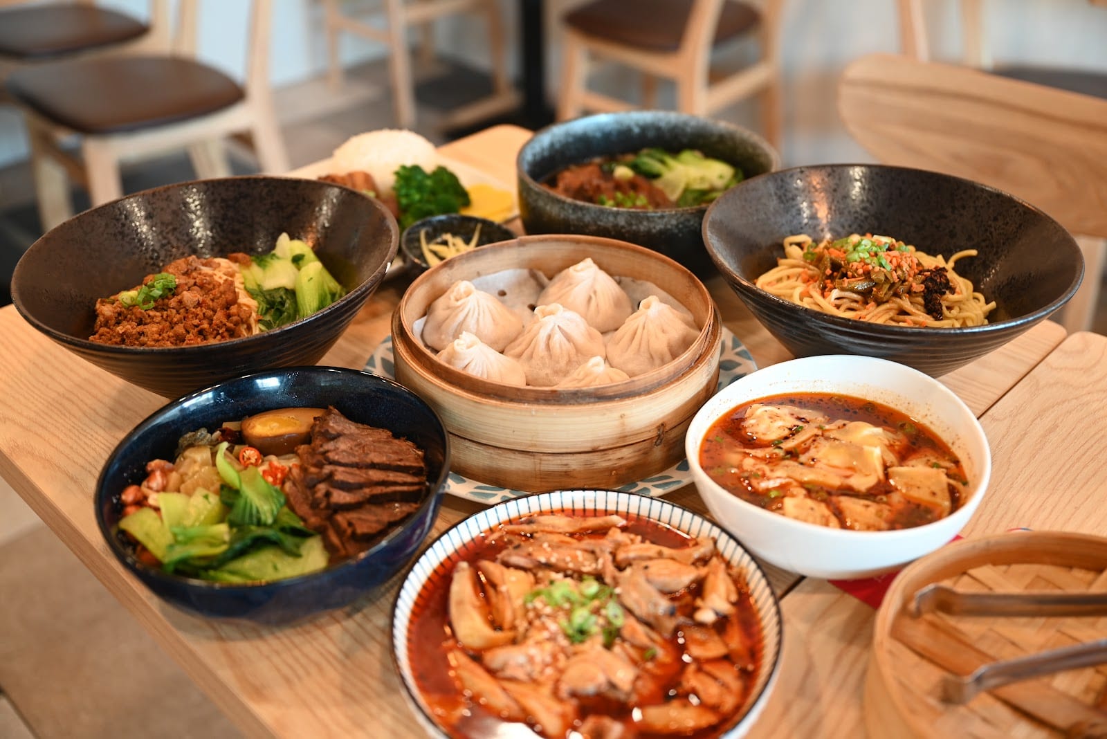 A bamboo steamer basket of soup dumplings with dipping sauce on the side.