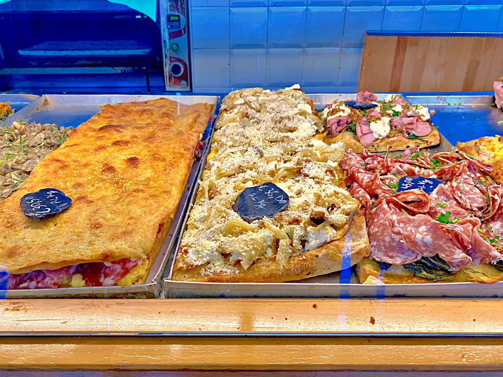 Trays of Roman pizza al taglio in the case at Bonci Pizzarium, cut and sold by weight.