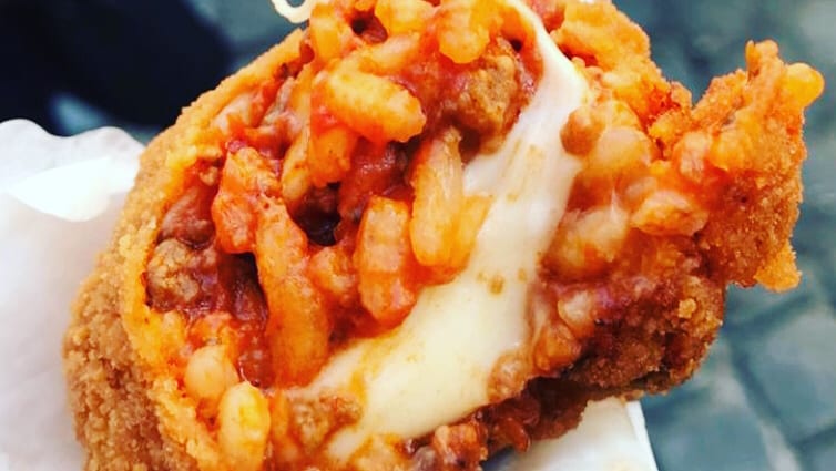 A suppli pulled open to show the tomato rice and the long string of melted mozzarella.