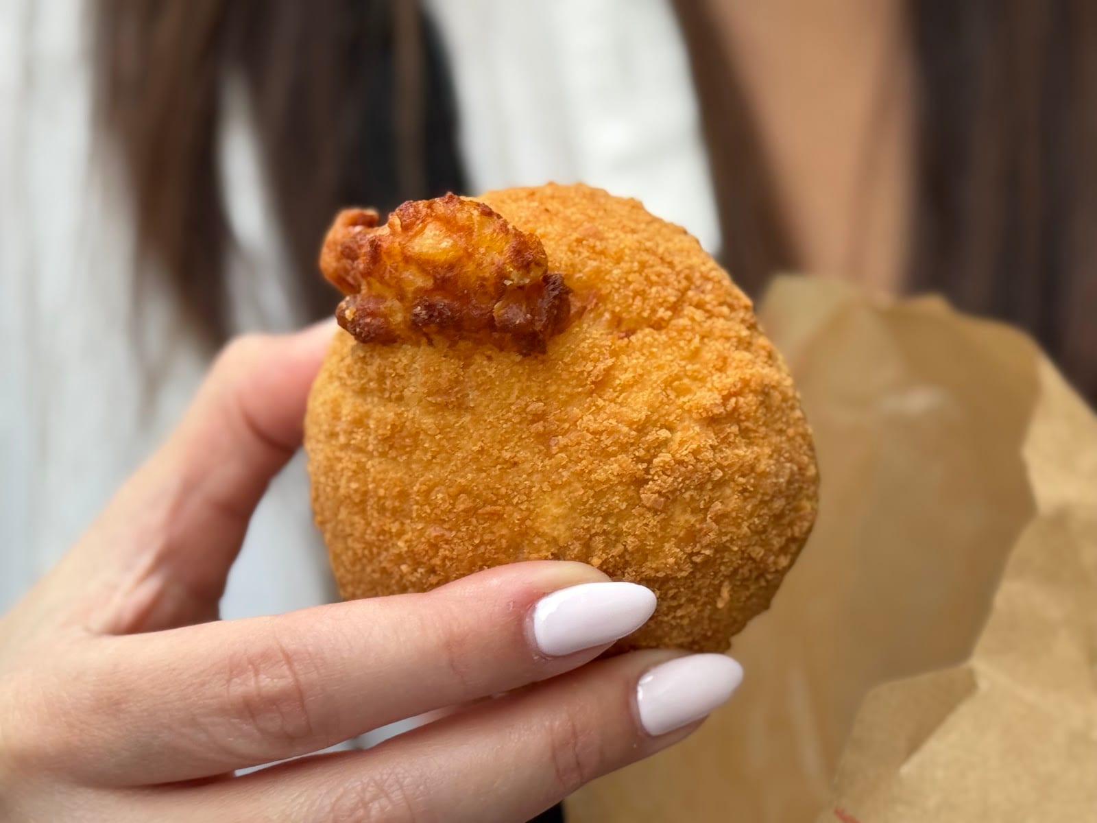A whole fried suppli held in hand, breadcrumbed and golden.