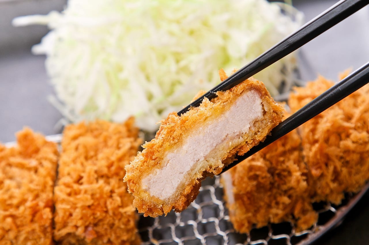 A panko-crusted pork cutlet held in chopsticks, showing the juicy cross-section, at Tonkatsu Maisen.