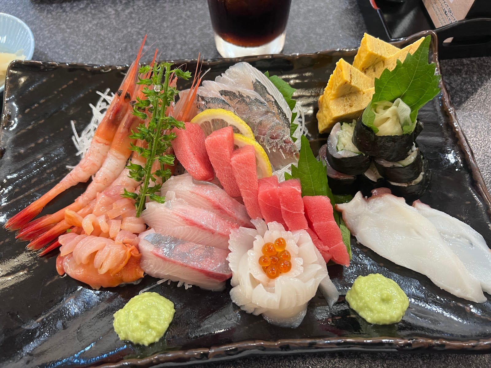 A platter of assorted sashimi and nigiri with wasabi at a Sushizanmai counter.