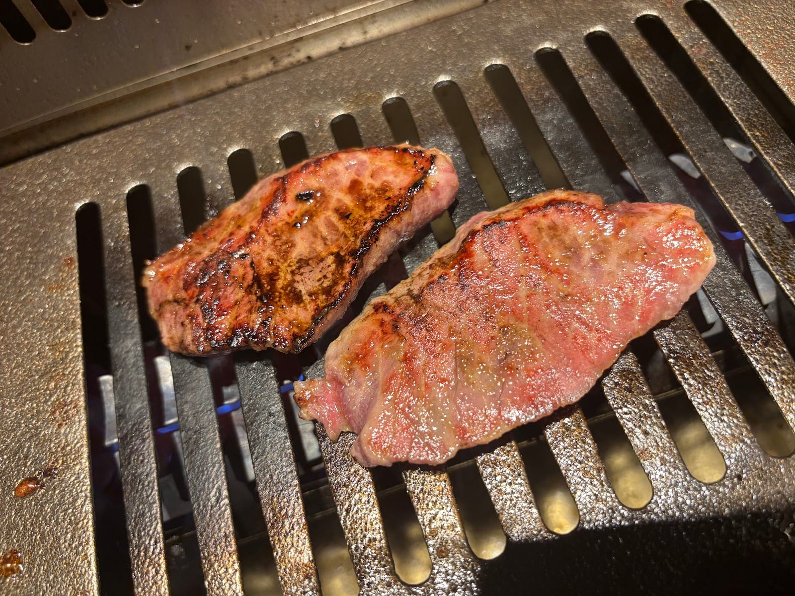 Cuts of wagyu searing over a charcoal grill at a yakiniku table.