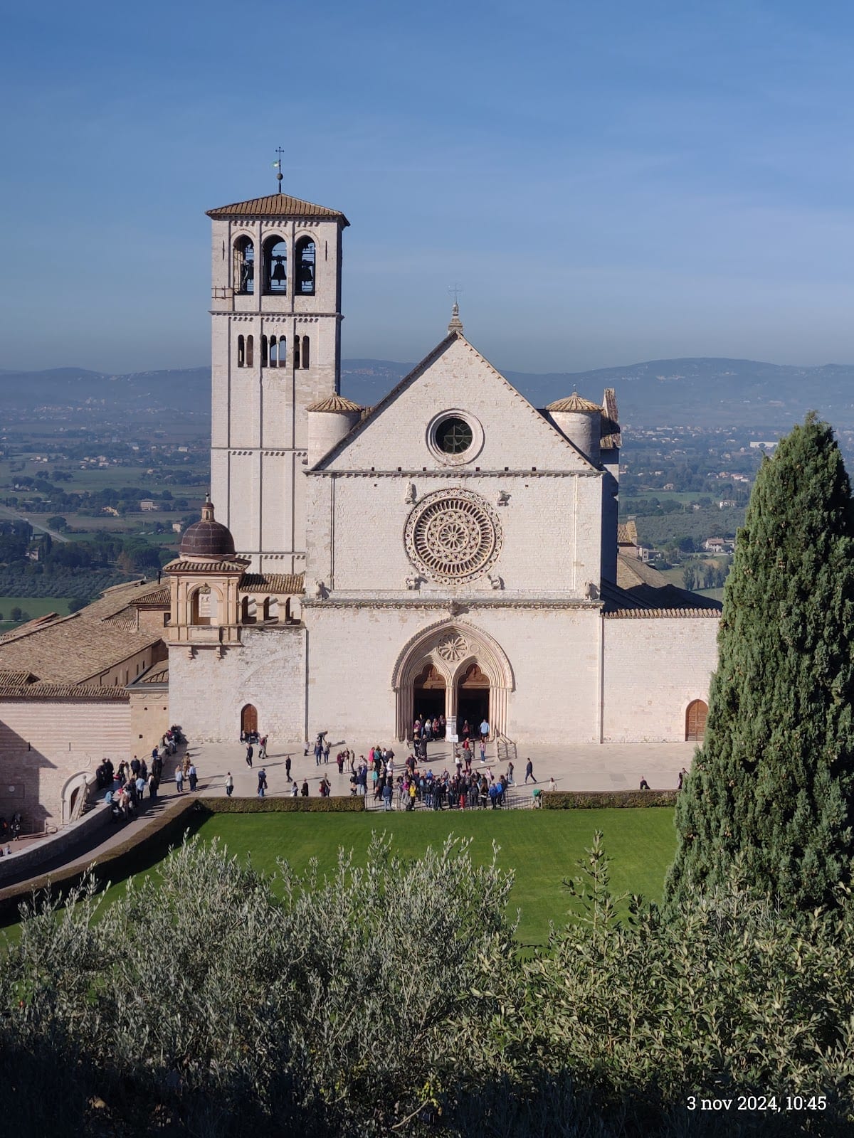The pink-stone facade and rose window of the Basilica of St Francis above the Umbrian valley.