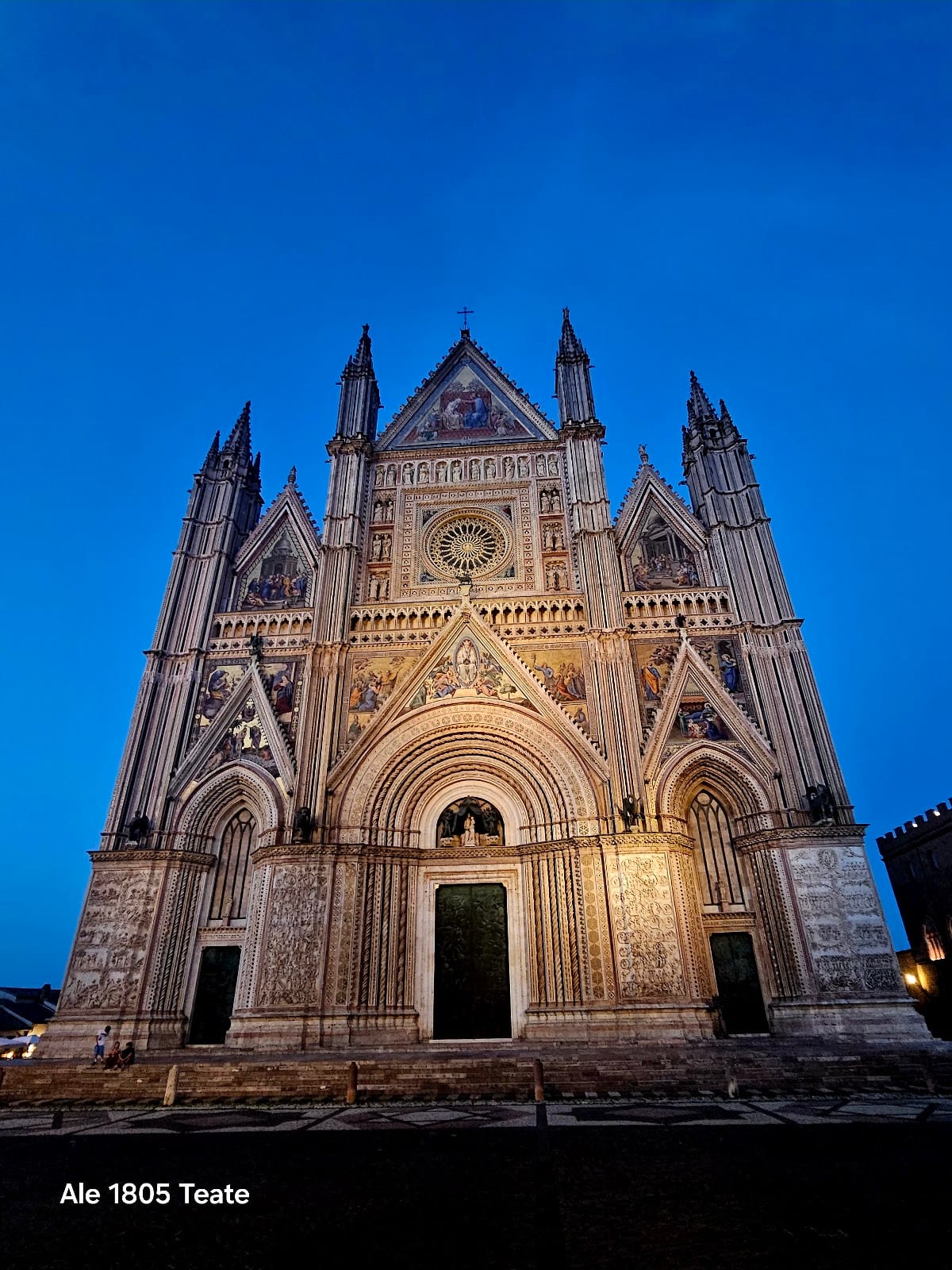 The striped gold-mosaic Gothic facade of Orvieto Cathedral glowing at dusk.