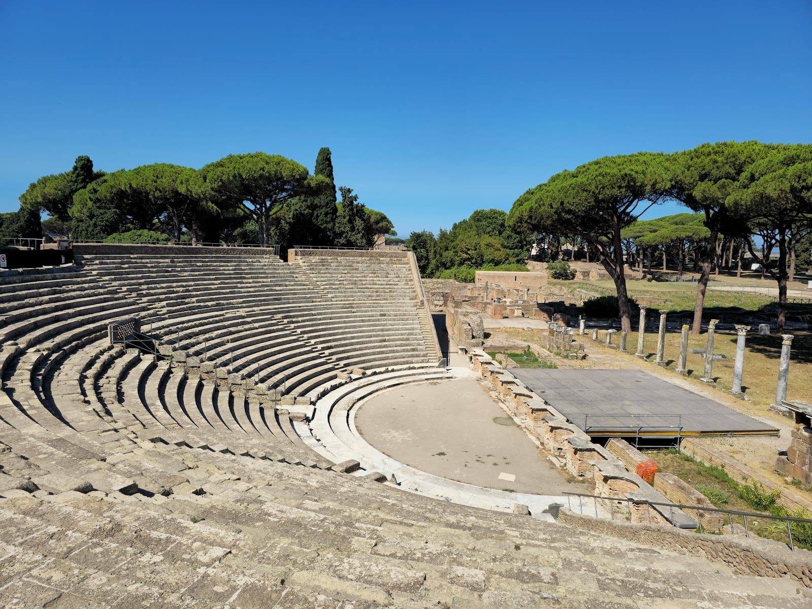 The stone tiers of the Roman theatre at Ostia Antica framed by umbrella pines.