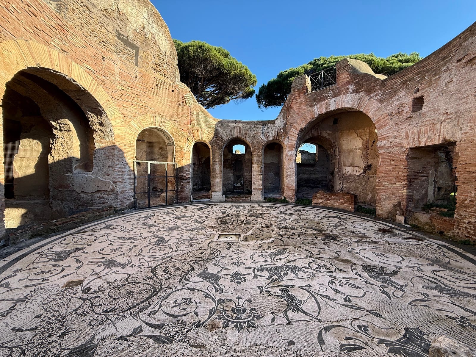 A floor mosaic beneath the brick arches of a ruined hall at Ostia Antica.