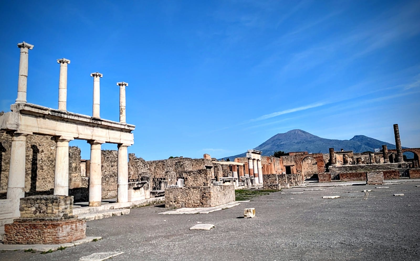 A row of standing columns and open ruins at Pompeii under a blue sky.