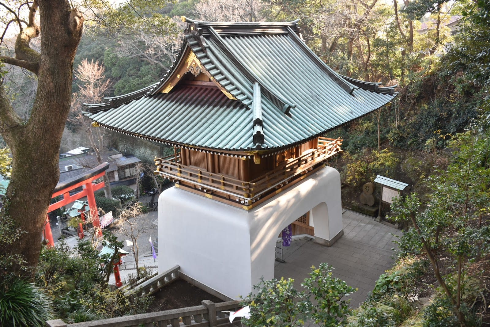 A green-roofed shrine pavilion among the trees on the hillside of Enoshima.