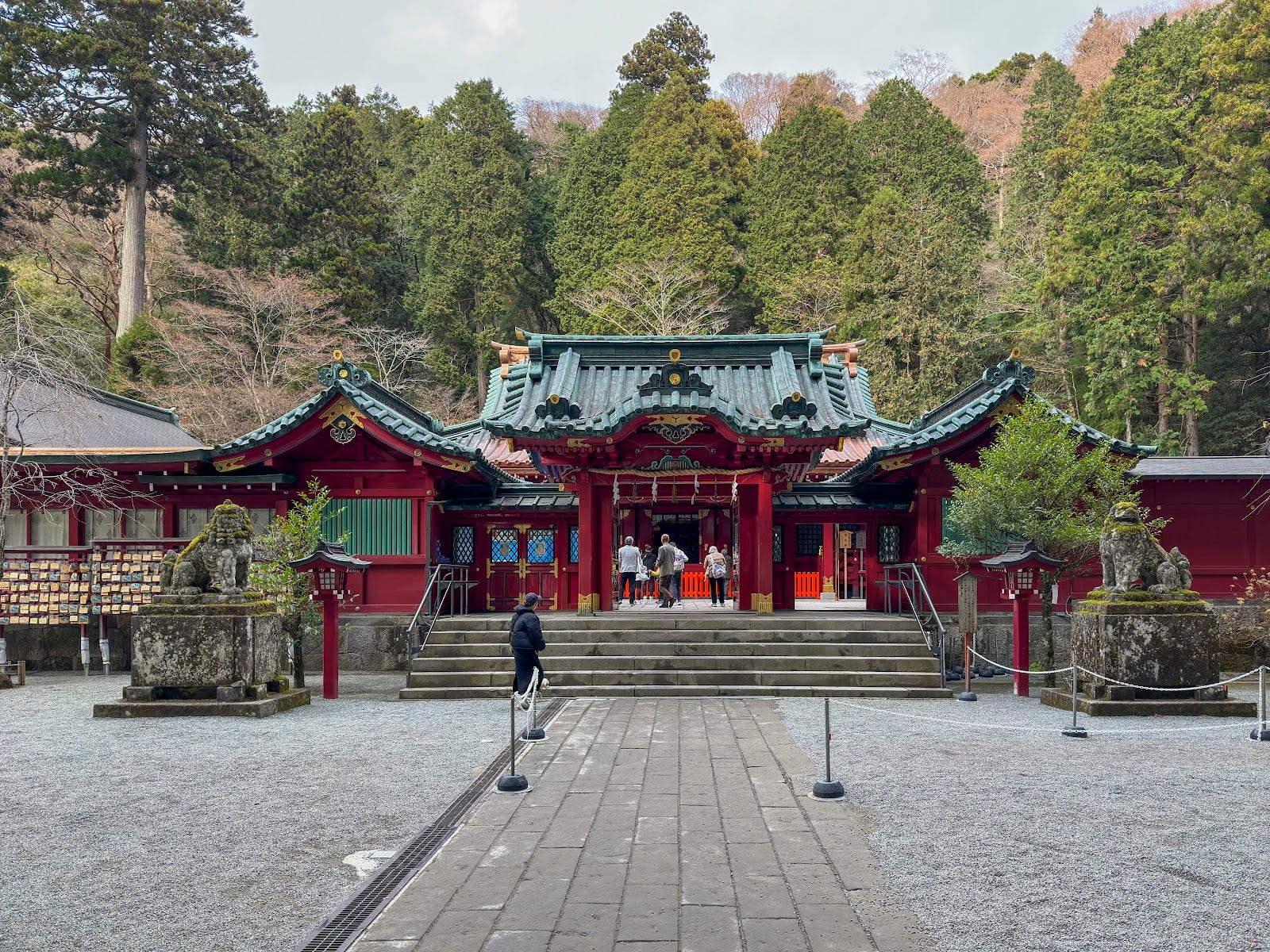 The green-and-vermilion main hall of Hakone Shrine among tall cedars.