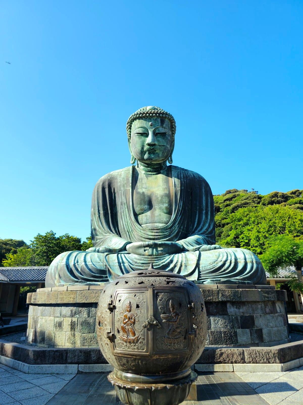 The Great Buddha of Kamakura, a giant weathered-bronze seated figure, against a green hillside.